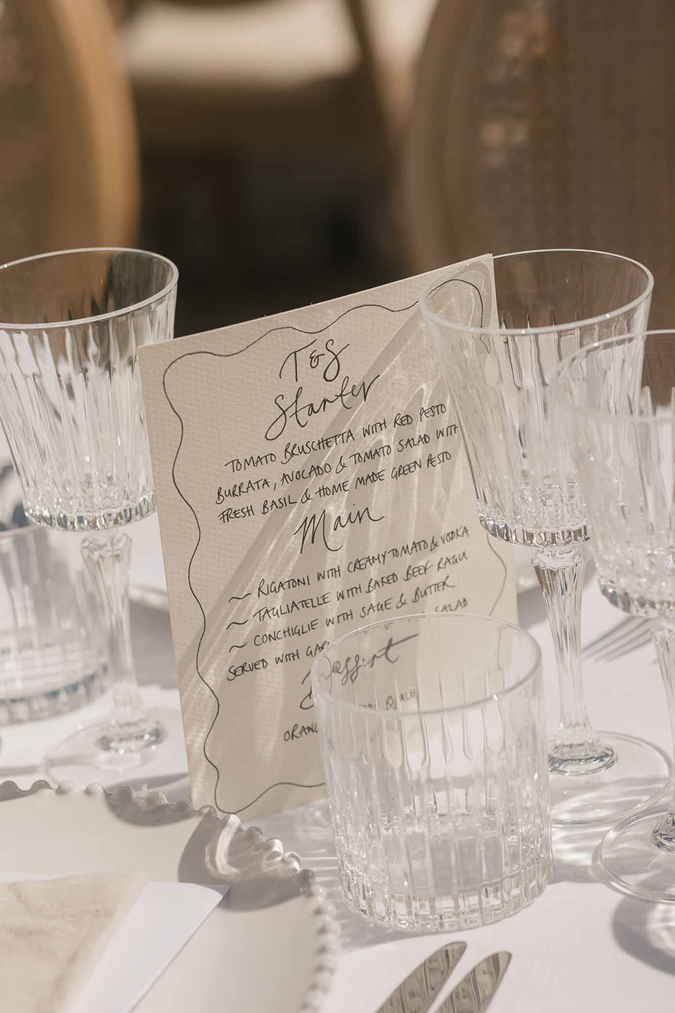 Handwritten calligraphy menu card with Italian courses beside faceted crystal glassware and pearl napkin ring