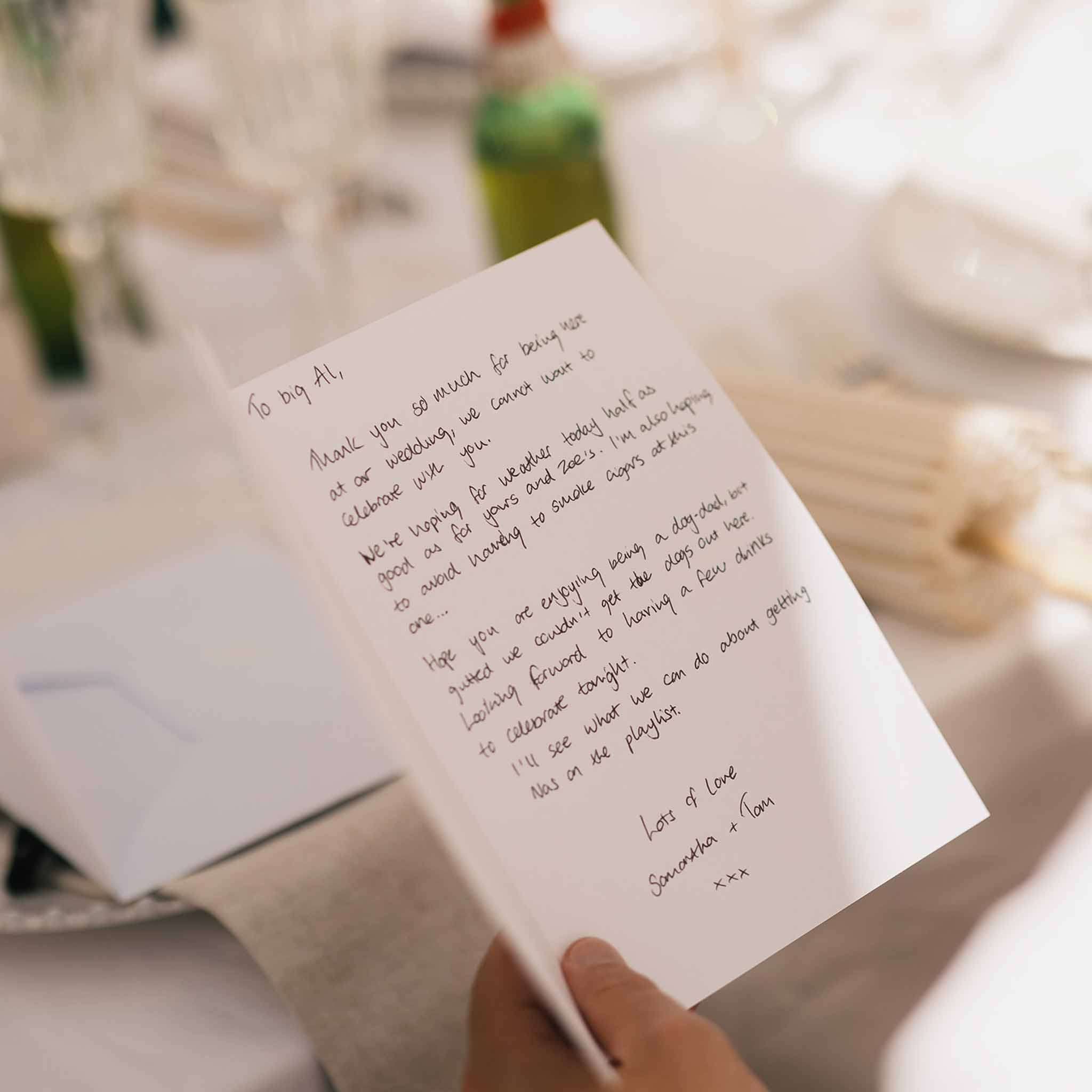 Close-up of a handwritten thank-you note from the couple to a guest at a reception table setting
