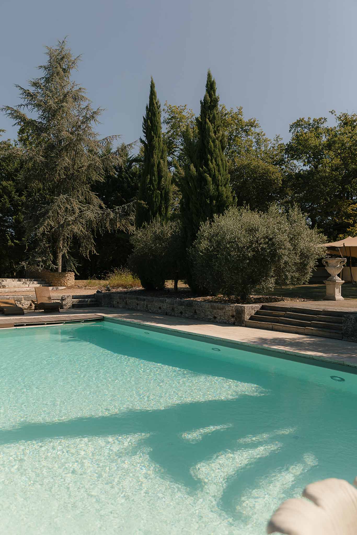 Rectangular turquoise pool with stone terrace, retaining walls, and classical urn planter at country estate