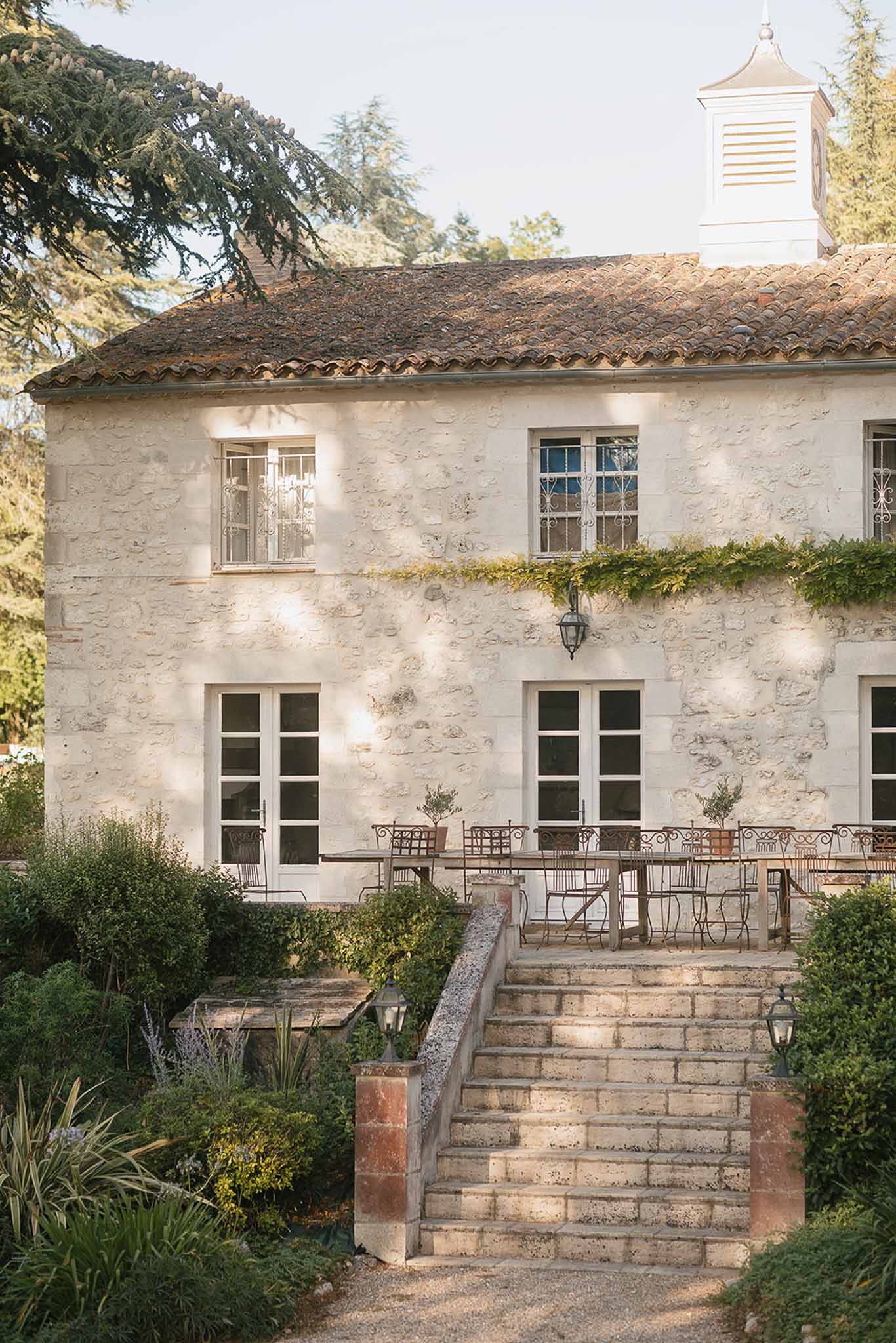 French country manor with cream limestone walls, terracotta roof, and stone staircase leading to furnished terrace