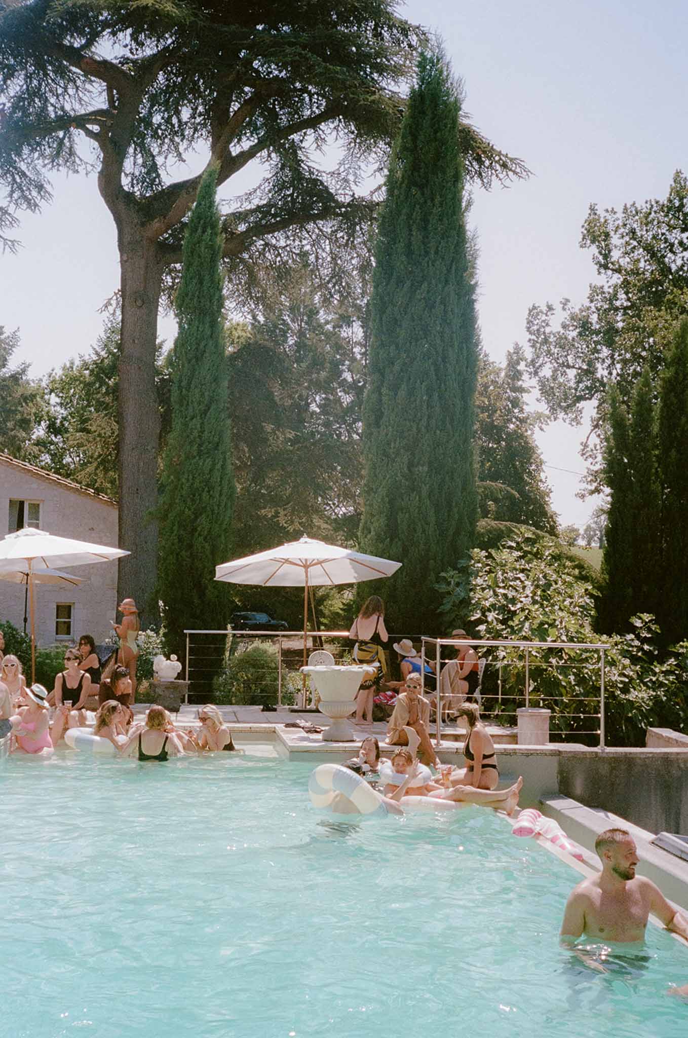 20 guests at pool party with striped inflatables and cream parasols at French country estate