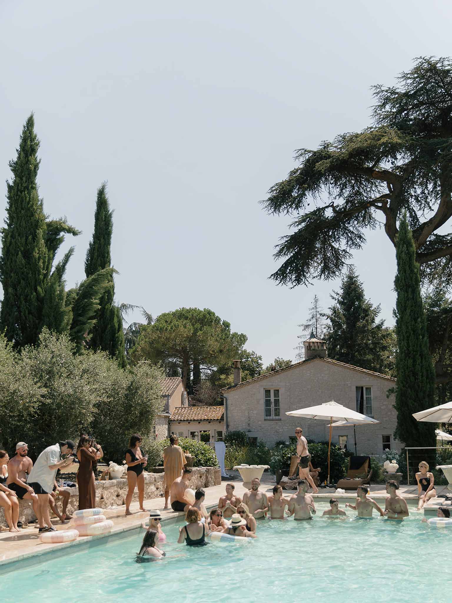 25 guests at pool party with pastel inflatables beside Provencal stone mas with terracotta roof