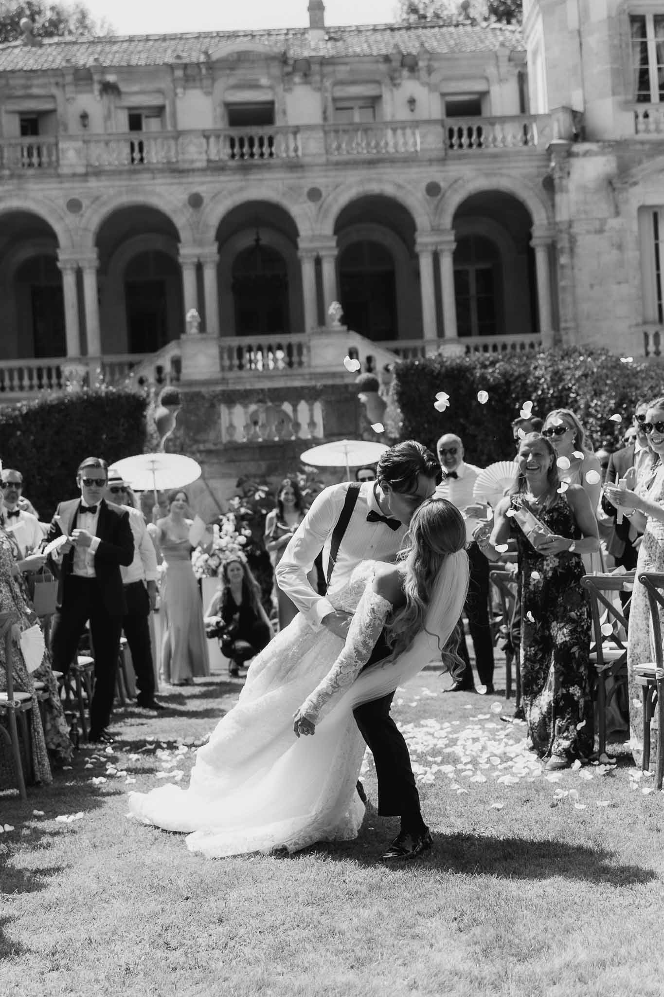 Black and white recessional dip kiss with petal toss at French chateau outdoor ceremony with colonnade backdrop