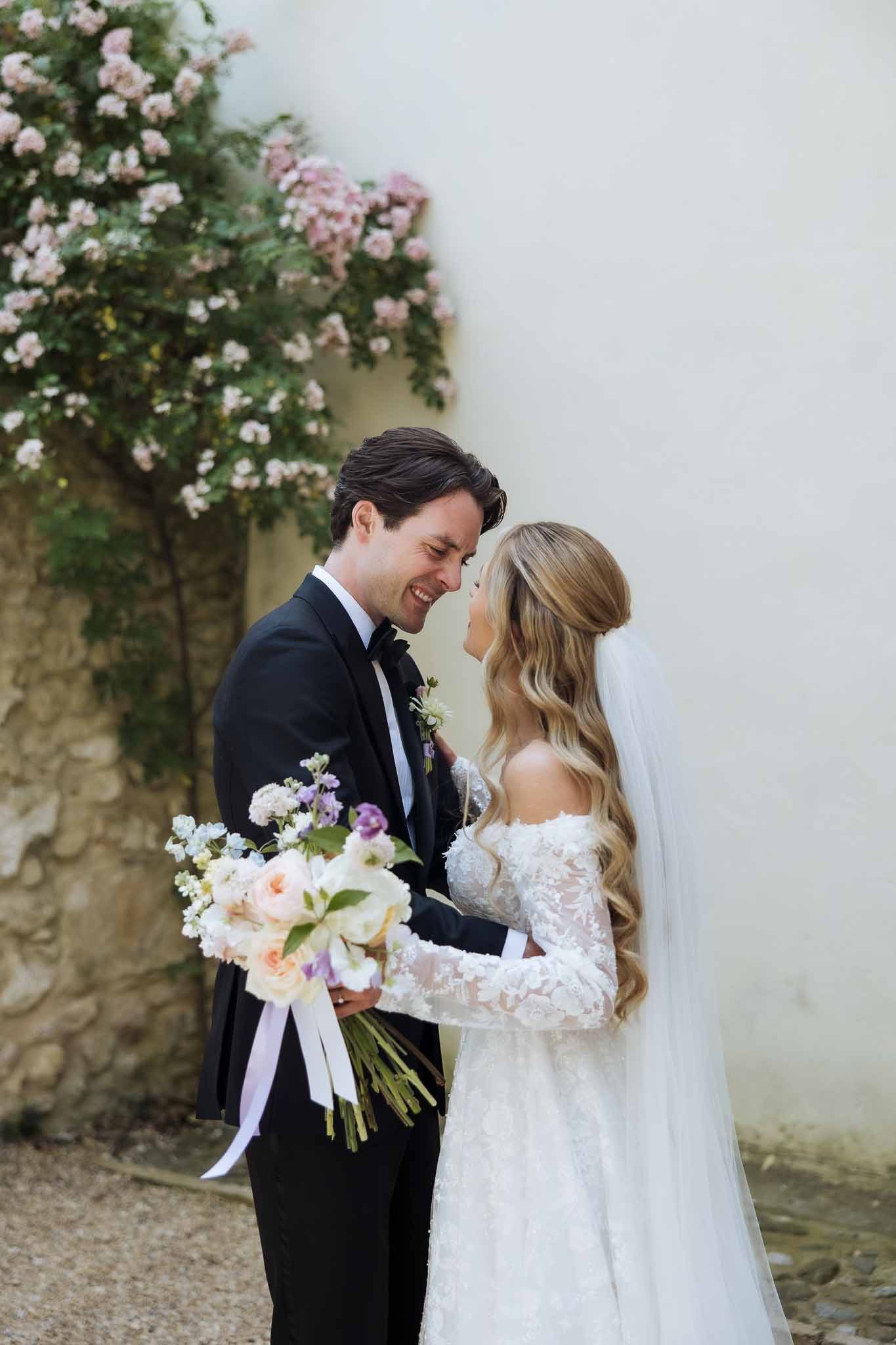 Couple touching foreheads as bride holds garden-style bouquet of blush roses and lilac stock