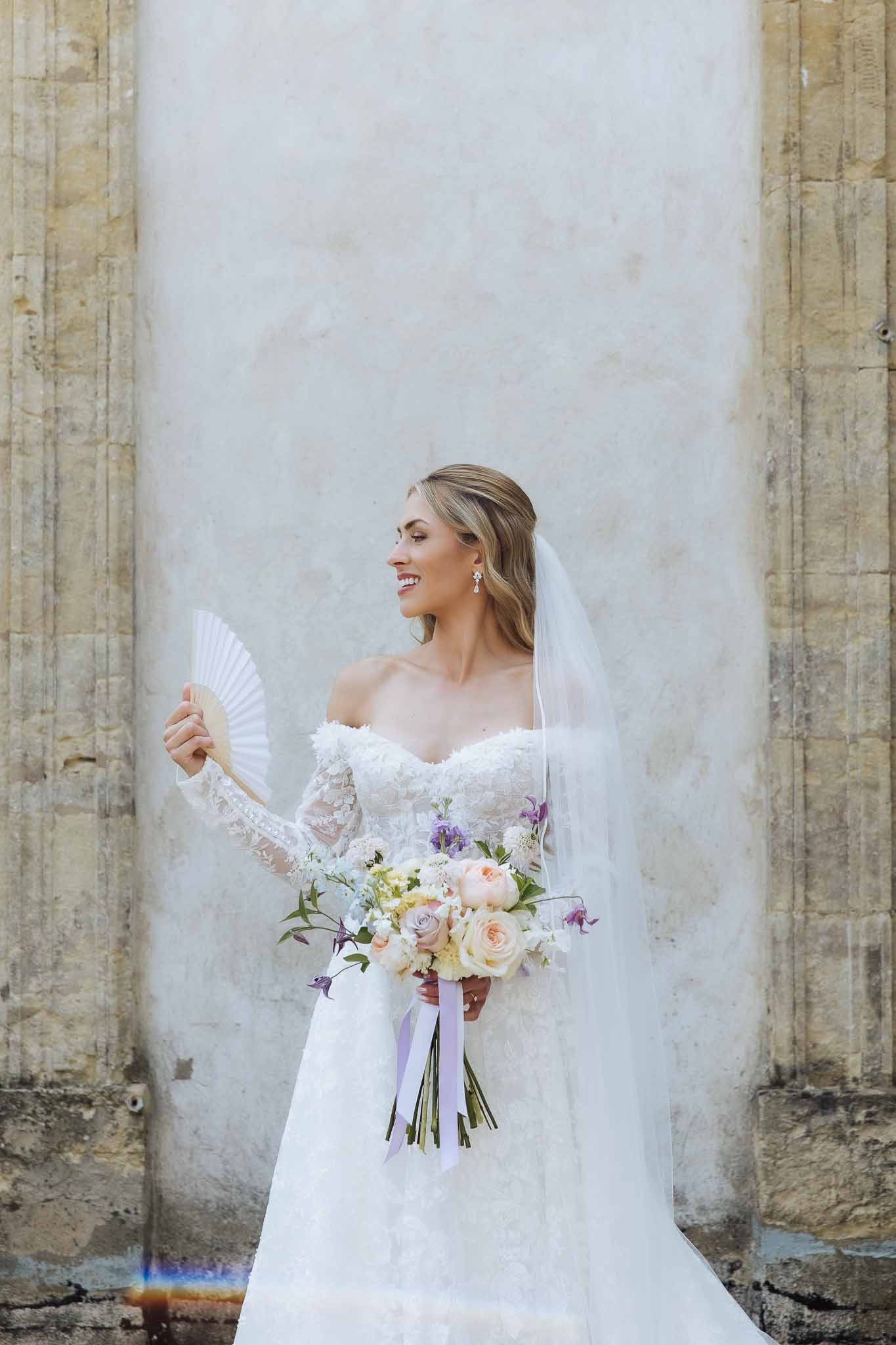 Bride in off-shoulder lace gown holding garden bouquet of roses sweet peas and scabiosa