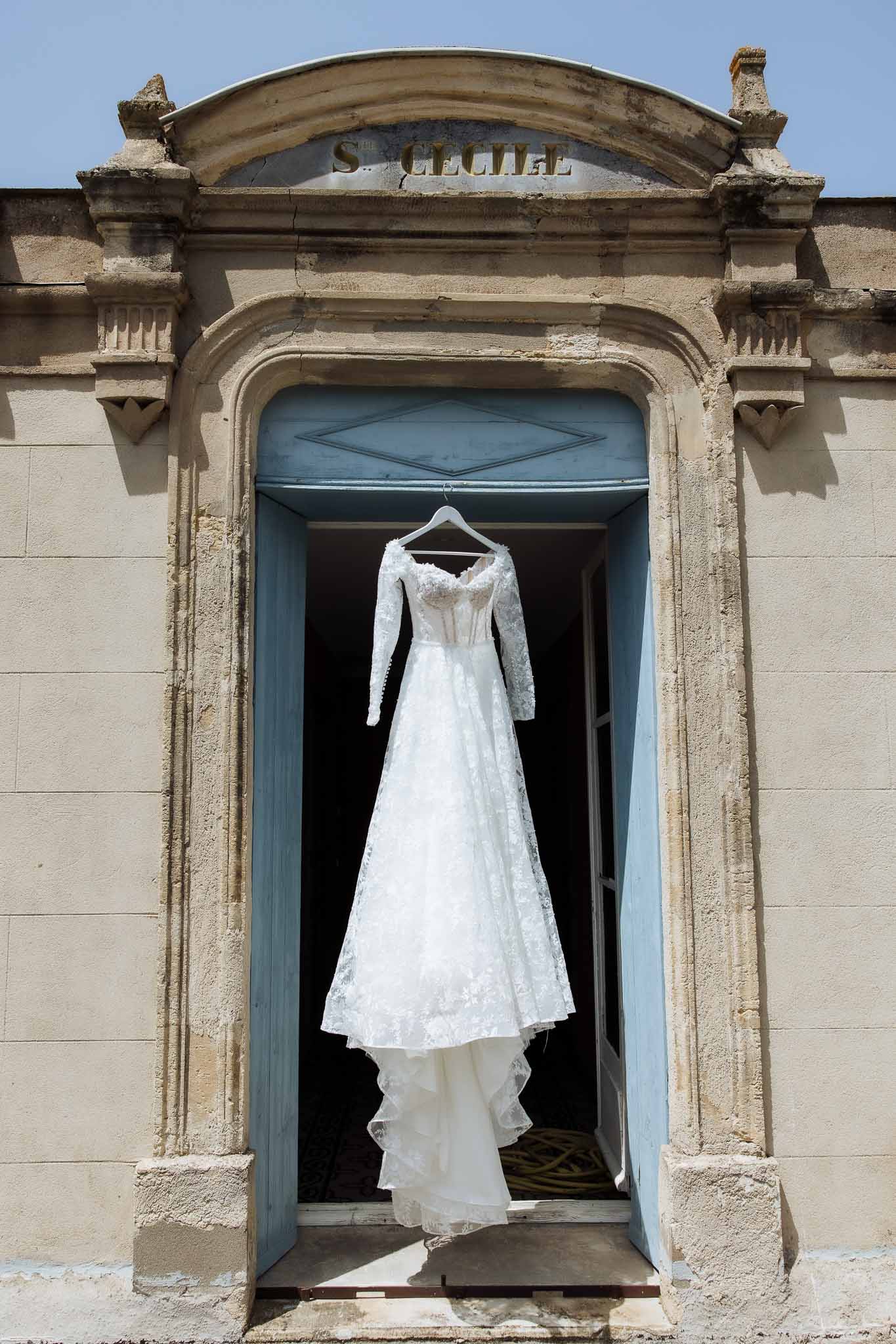 White lace wedding dress with long sleeves hanging in stone doorway inscribed S. Cecile with pale blue doors