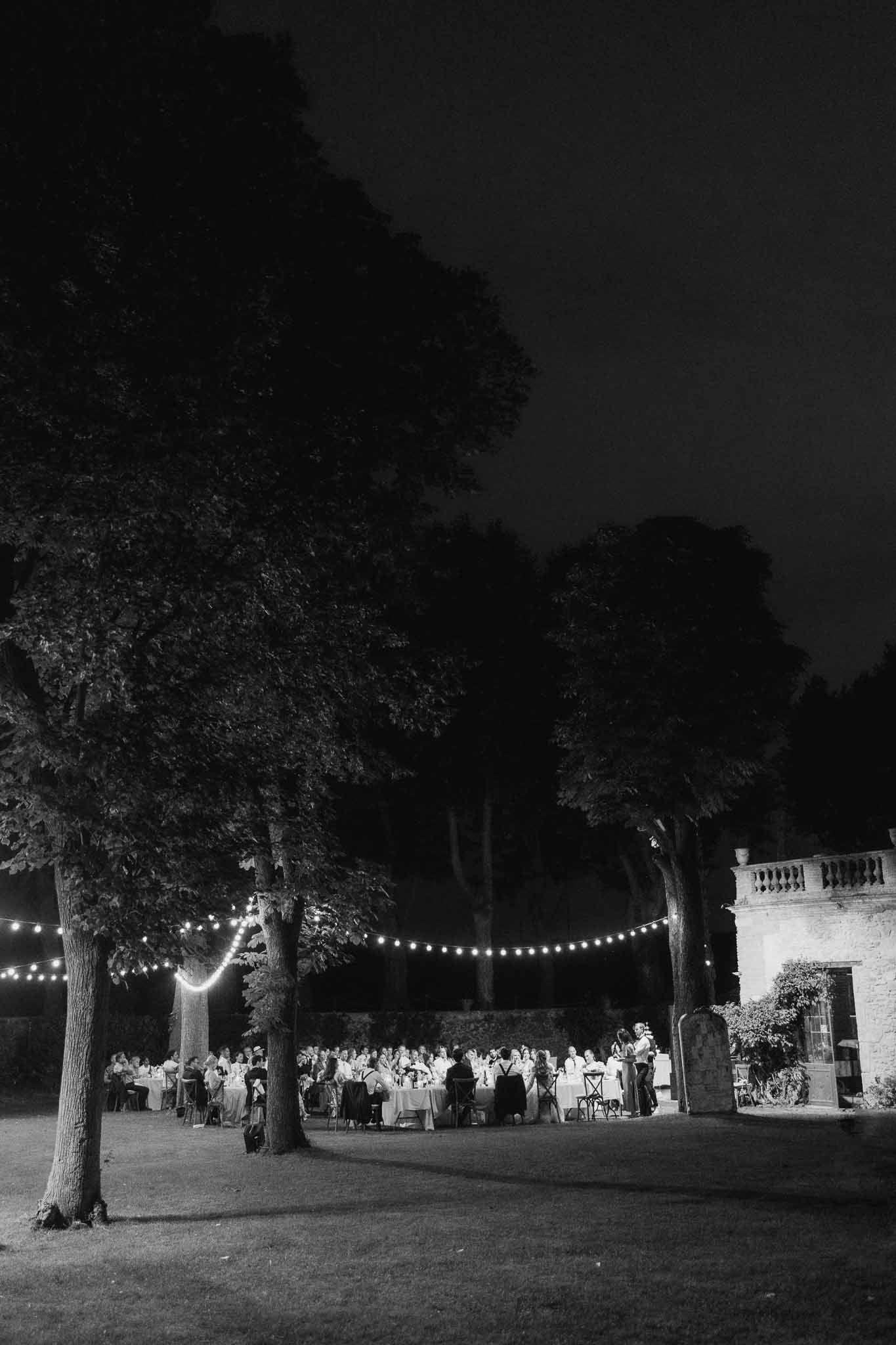 Black and white wide shot of evening reception under string lights on chateau lawn with 80 guests