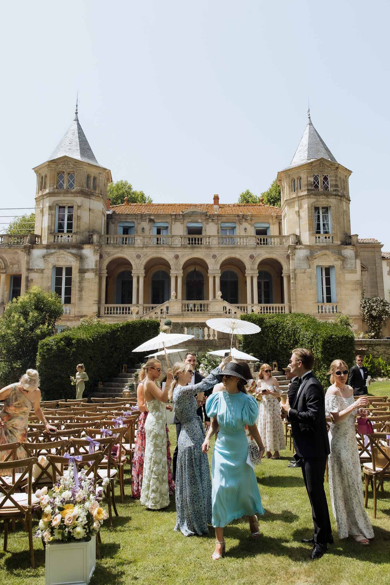 Outdoor chateau ceremony setup with wooden chairs, lavender ribbons, and yellow and white aisle flowers