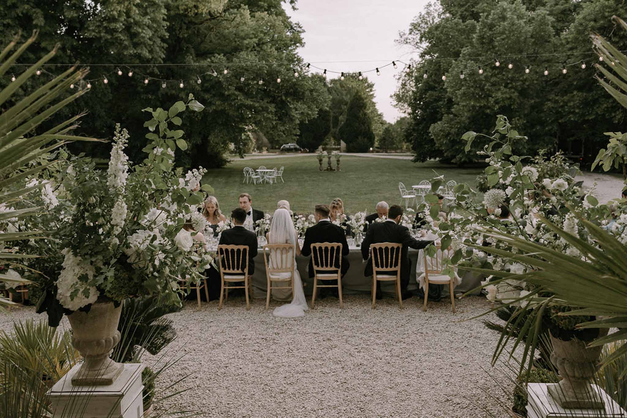 Outdoor reception dinner on terrace with sage green linens, white florals, and festoon lights at dusk