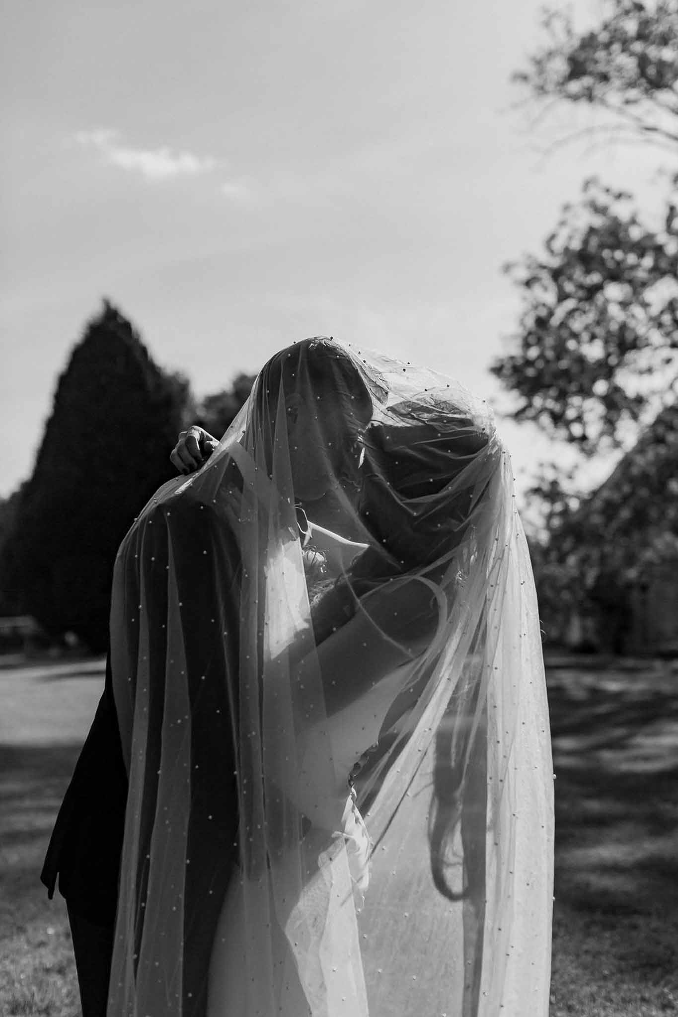 Black and white couple kissing beneath pearl-embellished cathedral veil draped over both figures