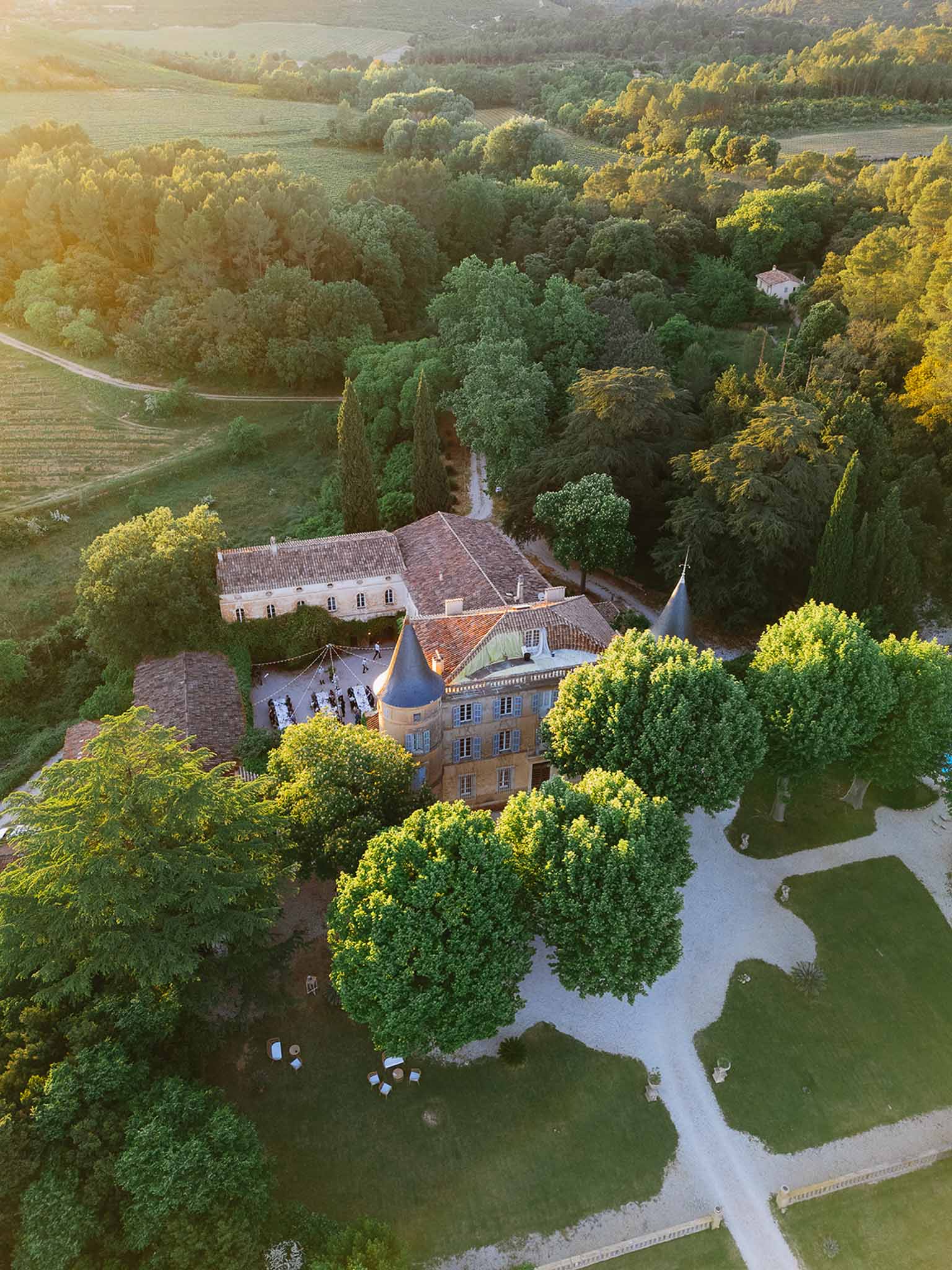 Aerial golden hour view of chateau with blue conical tower, courtyard reception, and vineyards