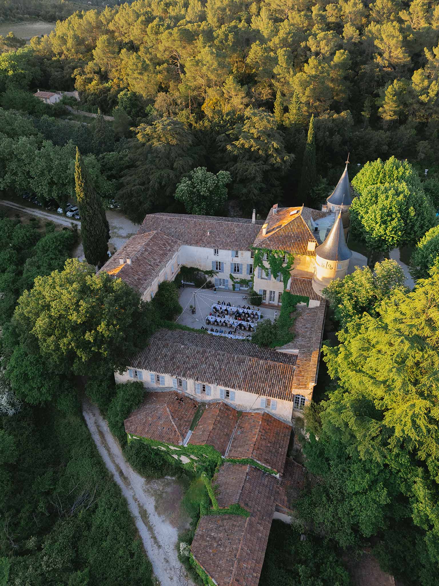 Aerial golden hour view of chateau with conical tower and courtyard reception for 70 guests amid woodland