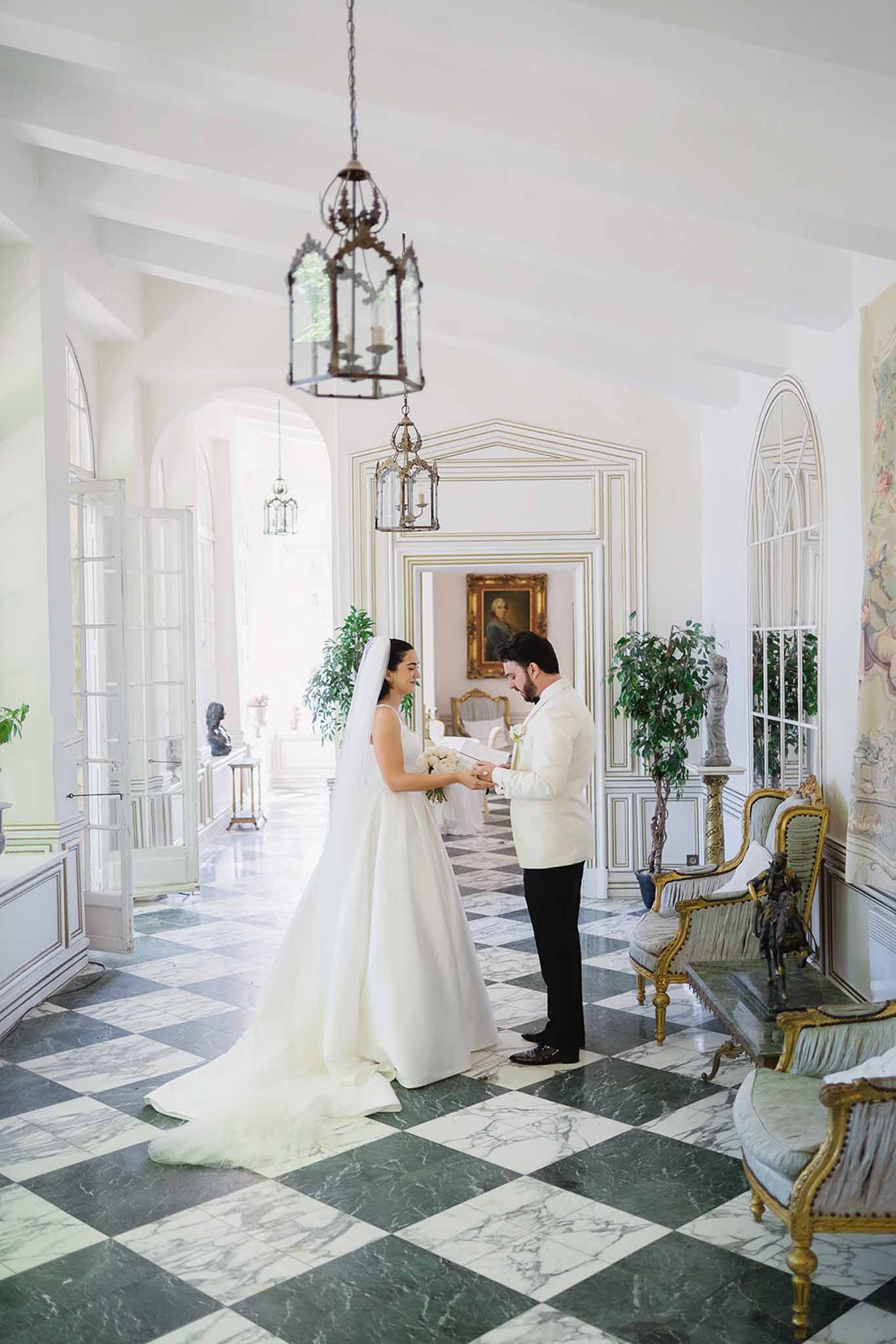 Couple holding hands in chateau gallery with checkerboard marble floor, gilt furniture, and lanterns
