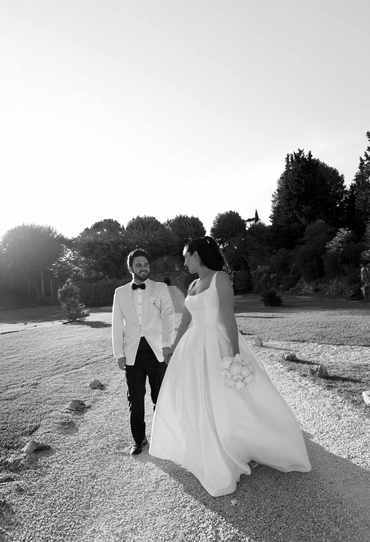 Black and white couple walking hand in hand on estate gravel path bride in full-skirted gown groom in white dinner jacket