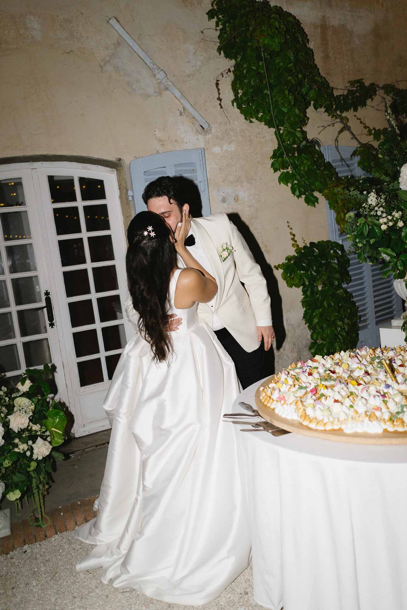 Bride and groom kissing beside piece montee wedding cake at outdoor evening chateau reception