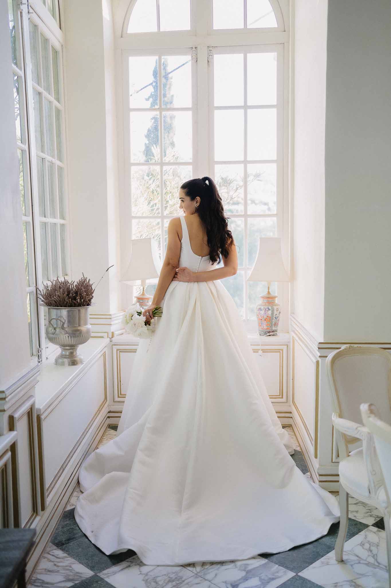 Bride glancing over shoulder in ivory ball gown with cathedral train in chateau room with arched windows