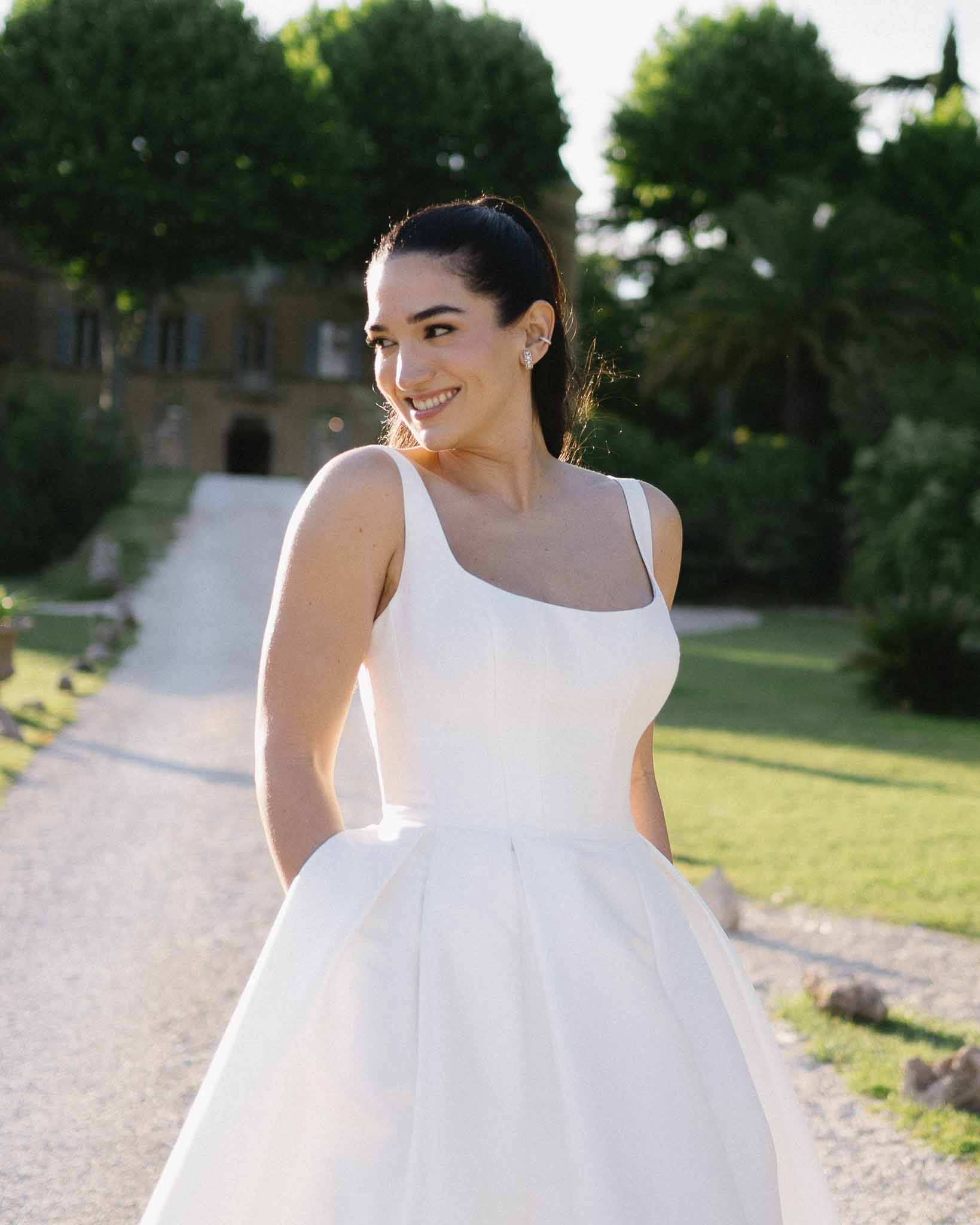 Bride in structured square-neck ball gown on gravel driveway with French chateau in background at golden hour