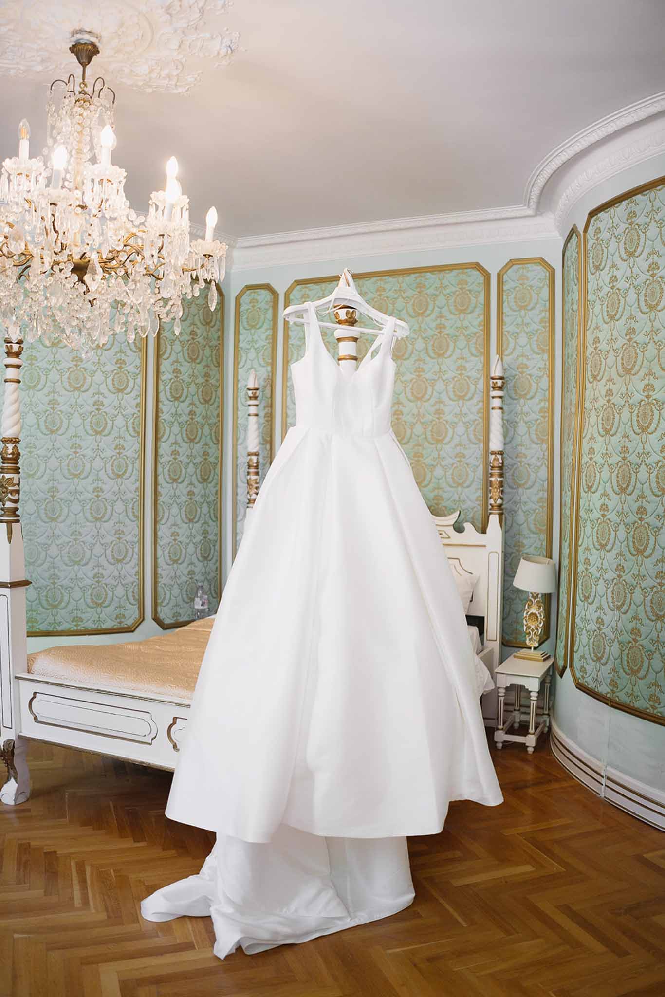 White ballgown with bow straps hanging from four-poster bed in sage green and gold damask panelled chateau bedroom