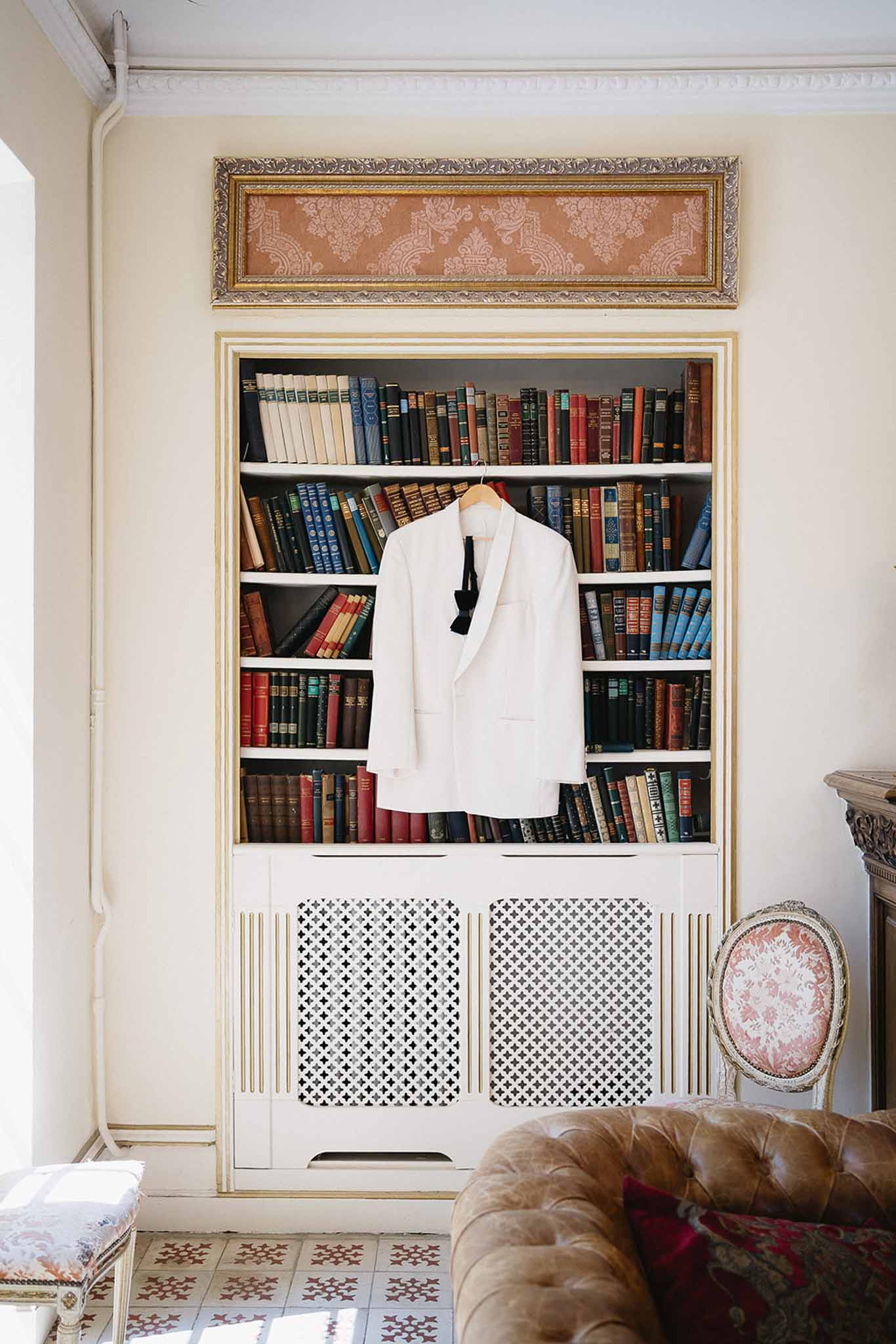 White dinner jacket with black bow tie hanging on bookcase of vintage hardcover books in chateau library