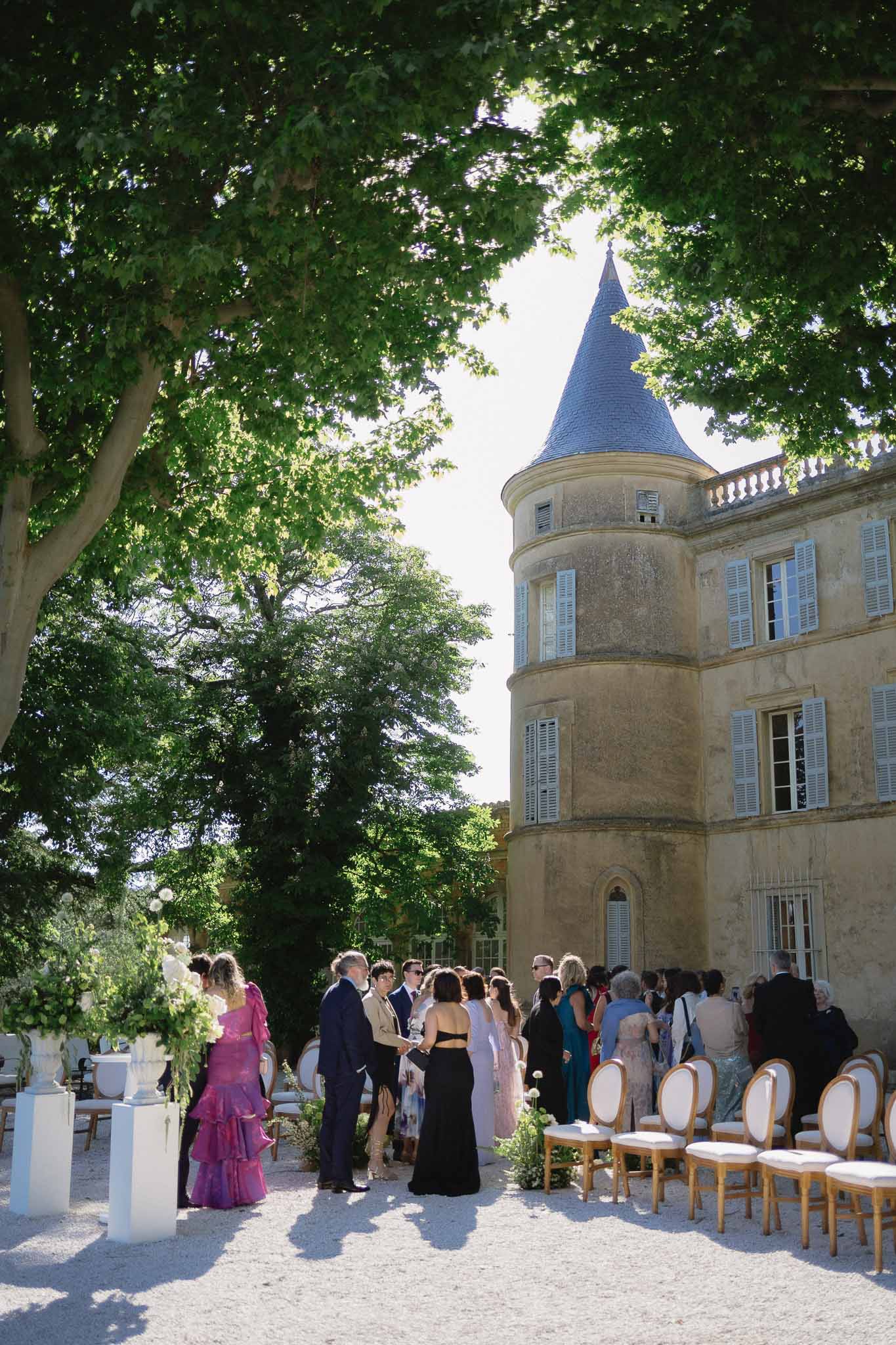 Guests mingling before ceremony with gold Louis XVI chairs and white pedestal florals at round-tower chateau