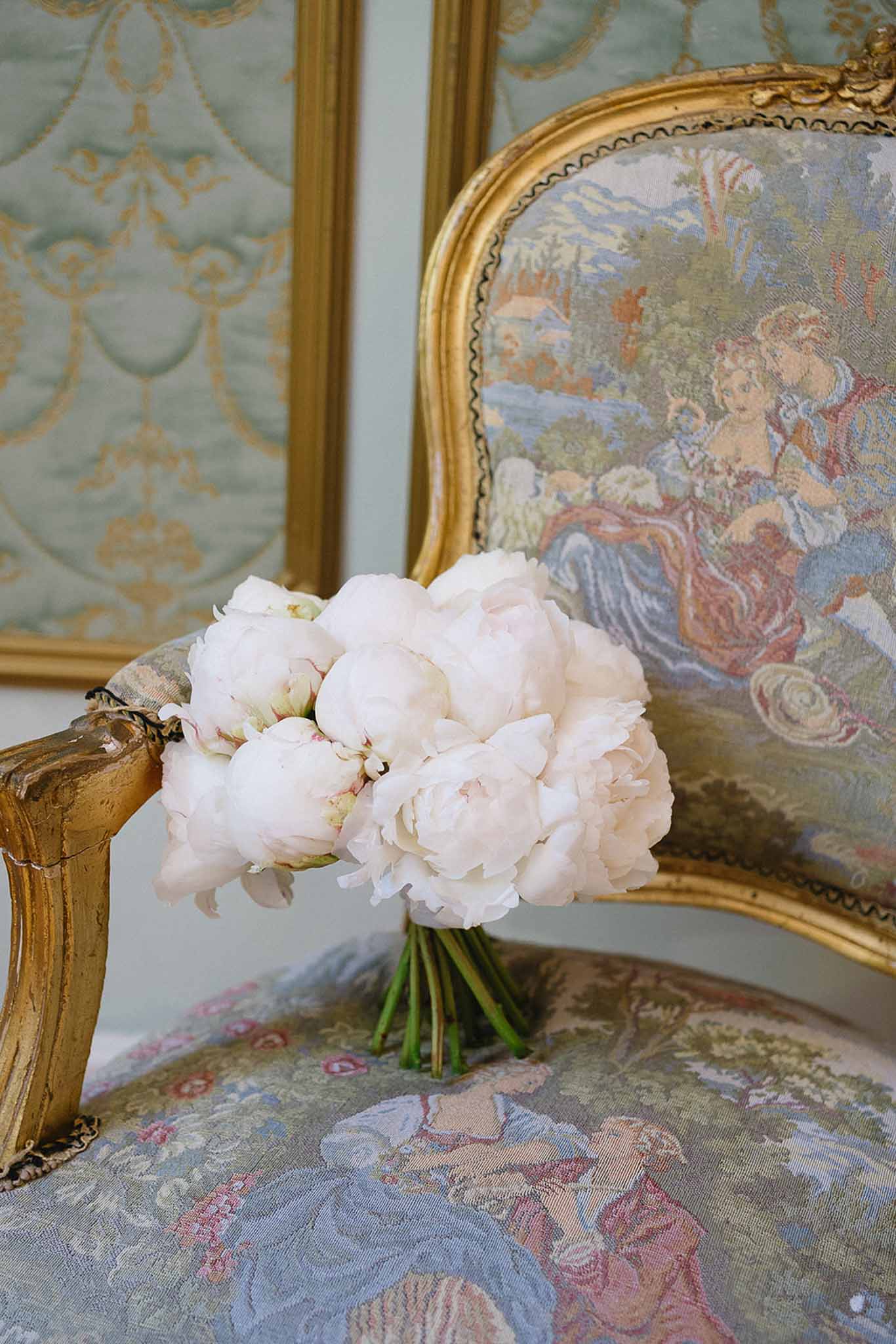 Blush pink peony bridal bouquet resting on gilt Louis XVI armchair with pastoral tapestry upholstery
