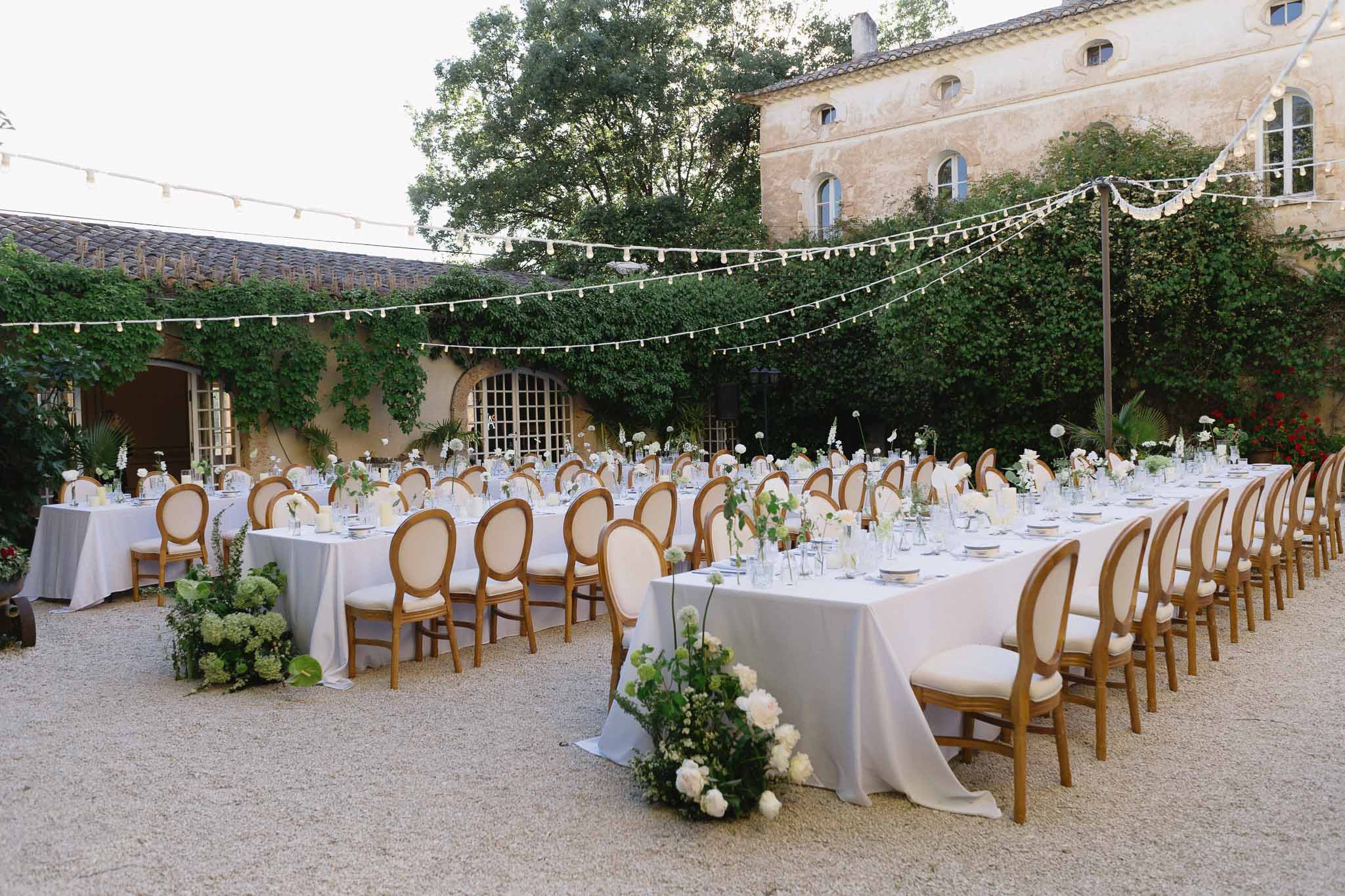 Long tables with white bud-vase florals and gold Louis XVI chairs under globe lights at stone manor