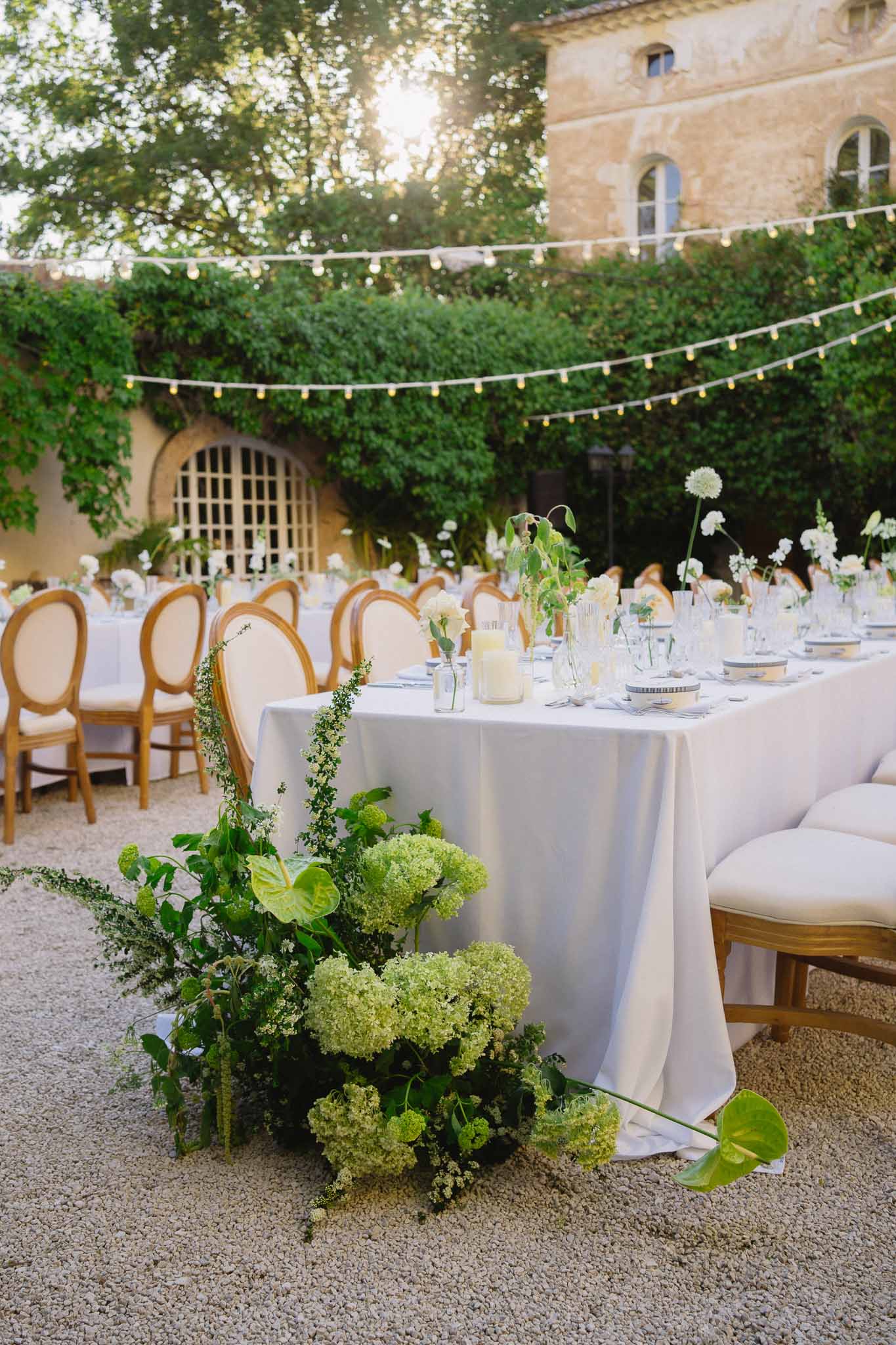 Outdoor chateau courtyard reception with grey-blue linen tables, green hydrangea installation, and string lights