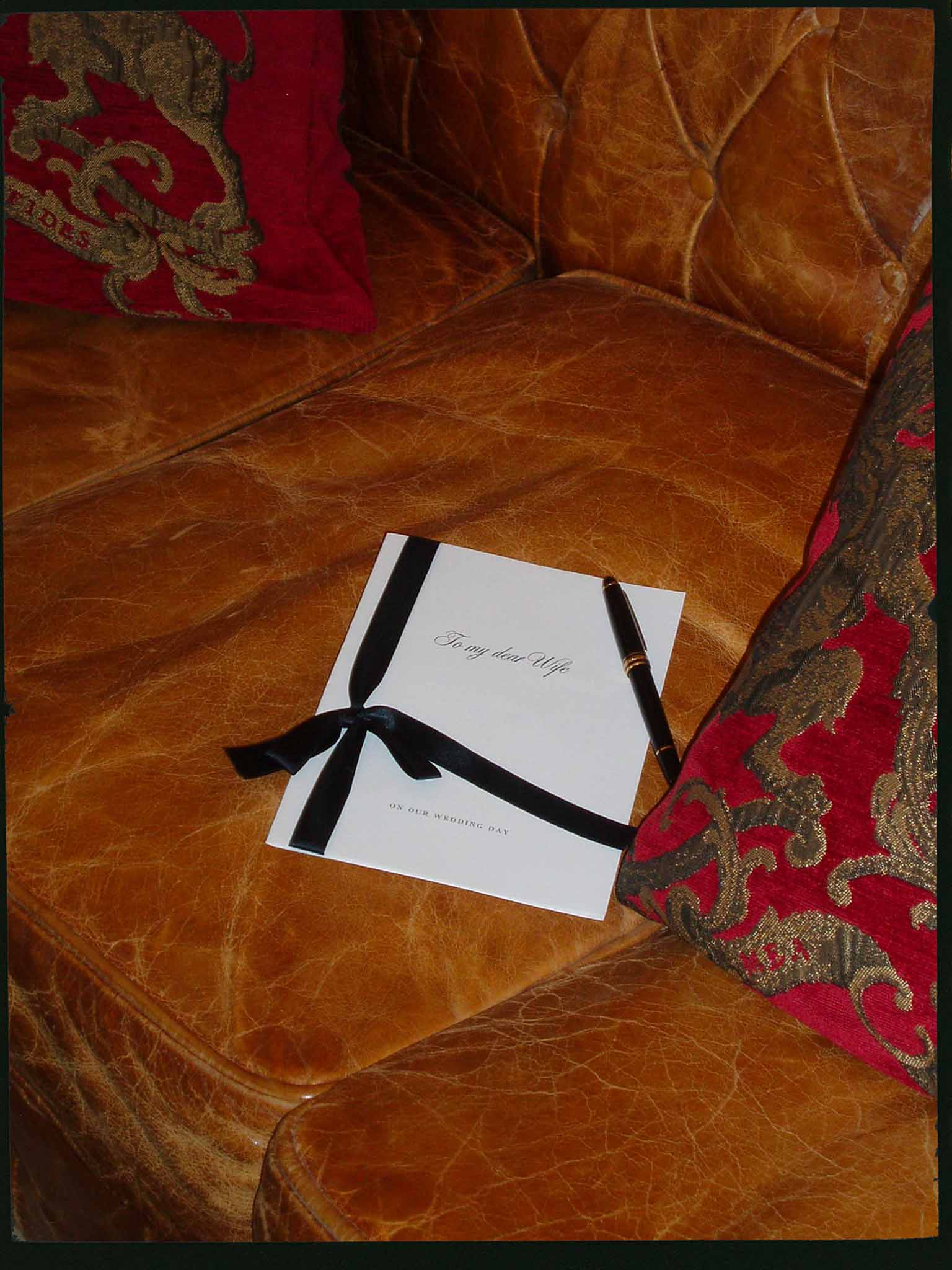 Wedding day letter to wife with black satin ribbon bow and fountain pen on tufted leather sofa