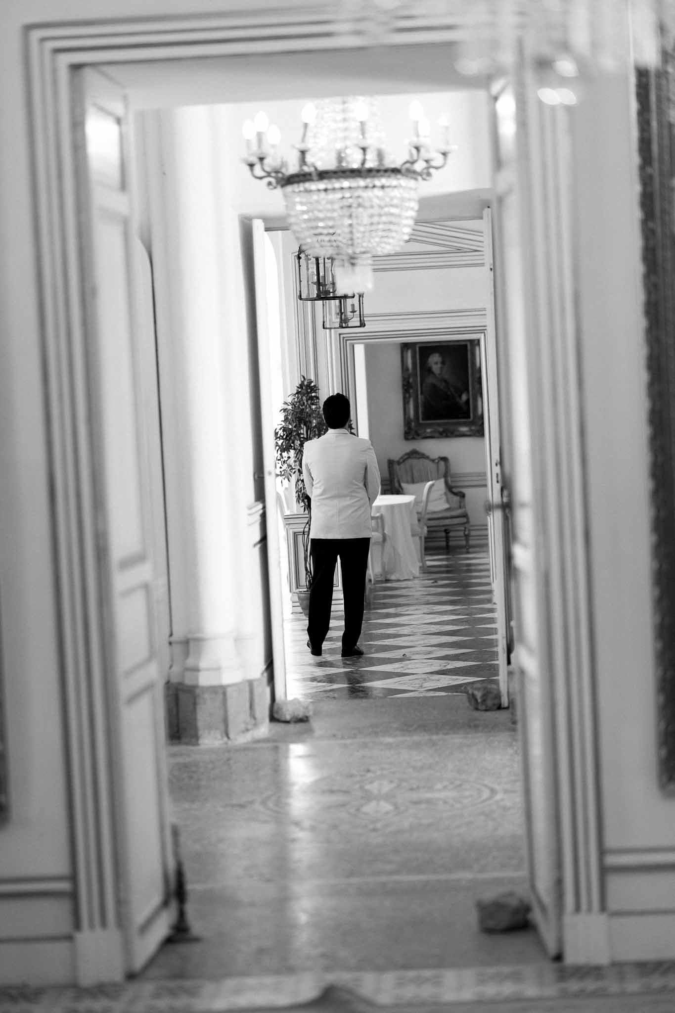 Staff member walking through ornate chateau doorway with crystal chandelier and checkered marble floor in black and white