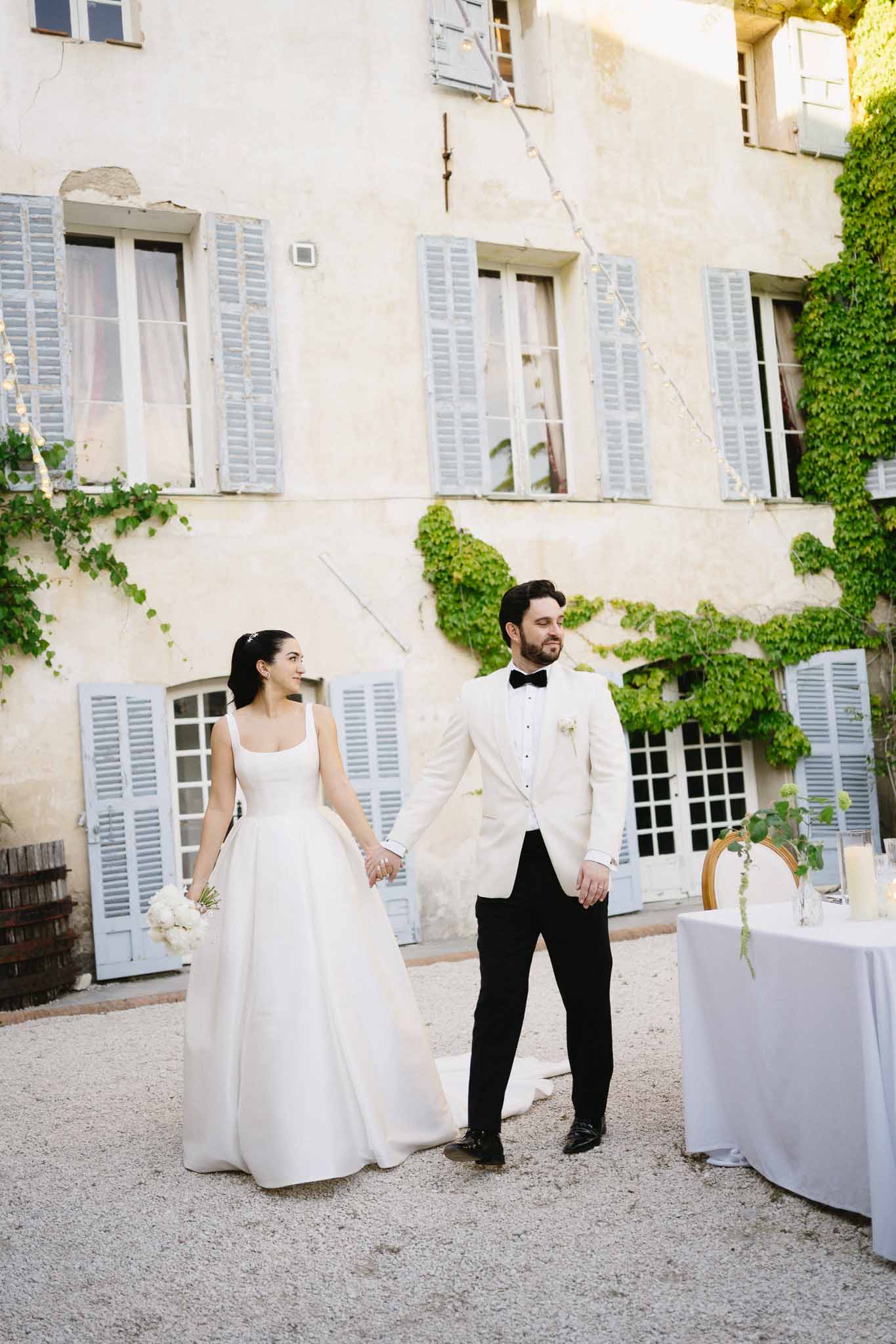 Bride and groom holding hands in chateau courtyard with climbing greenery backdrop