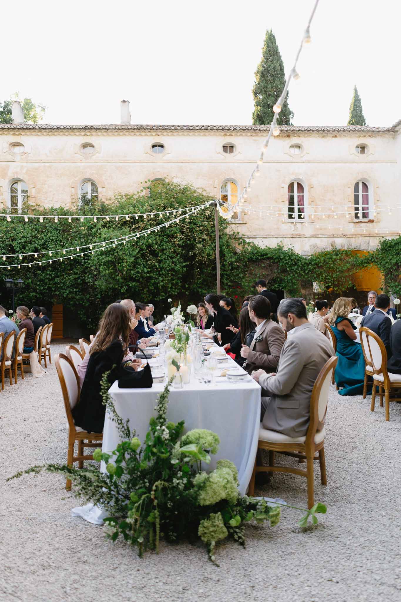 Outdoor reception dinner in manor courtyard with green and white florals and globe string lights