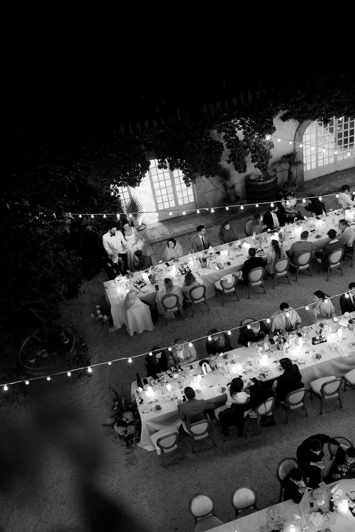 Aerial black and white view of outdoor night reception with three long tables lit by candles and fairy lights