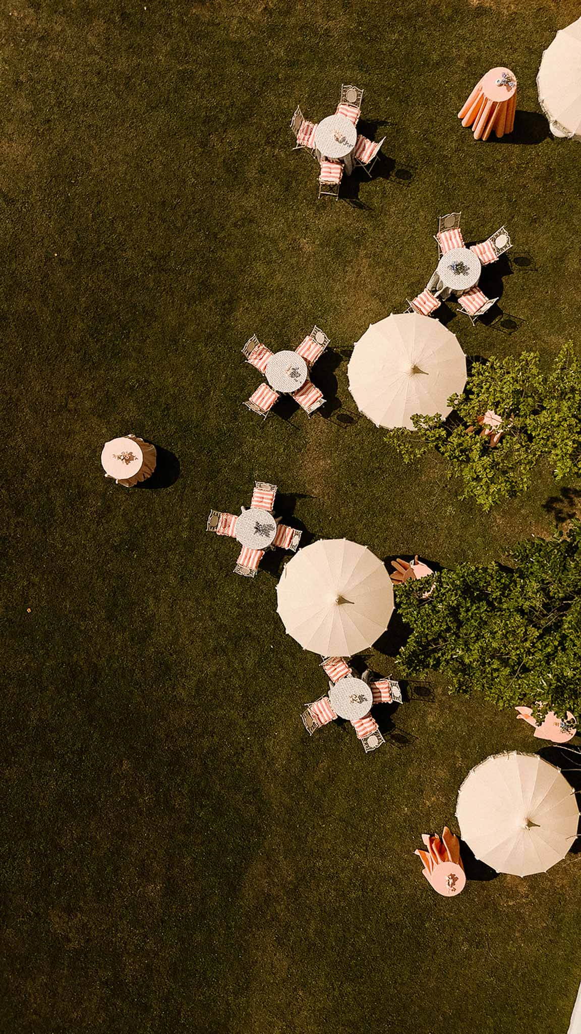 Aerial view of outdoor cocktail hour setup with round white tables and coral-striped cushions on a lawn