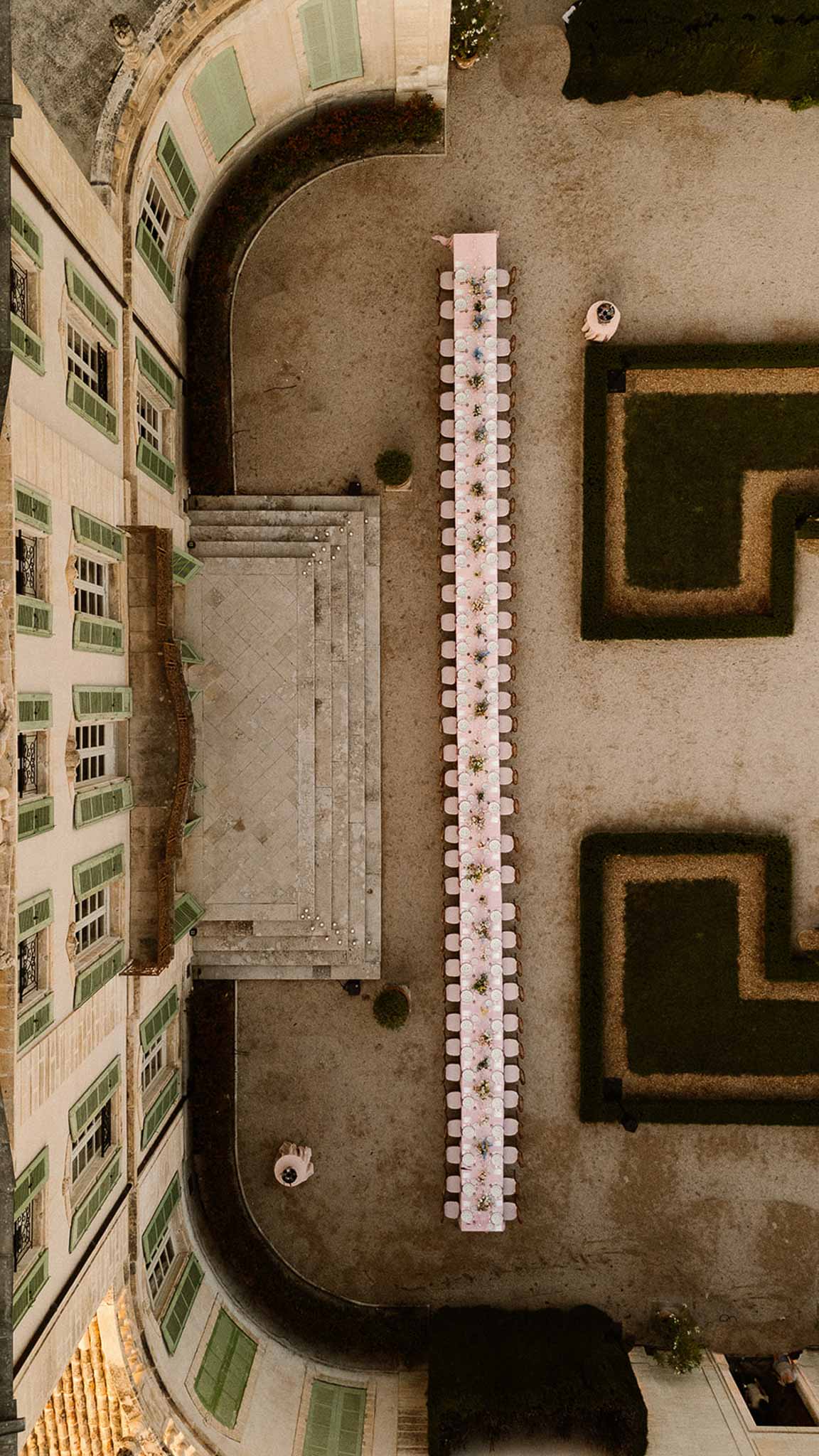 Aerial view of long banquet table in chateau courtyard with parterre gardens and stone facade