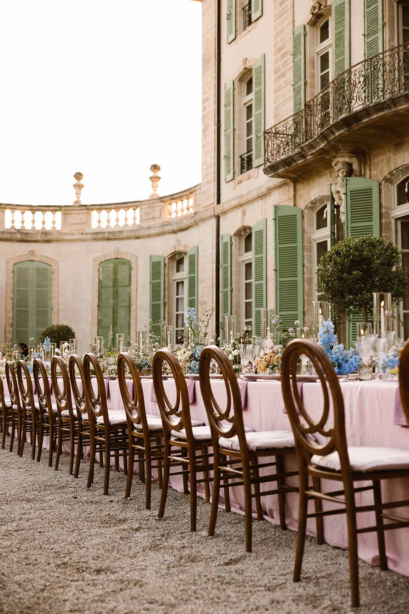 Blush linen banquet table with blue hydrangea and yellow topiary centrepieces before sage-shuttered chateau
