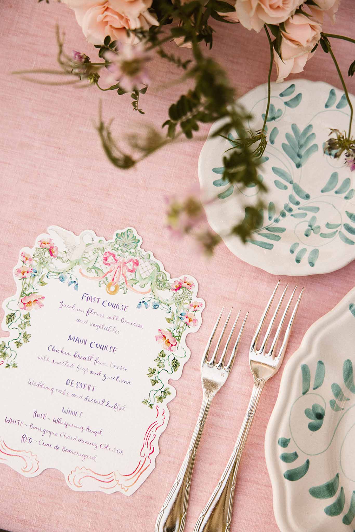 Illustrated rococo menu card with botanical plates, silver forks, and blush roses on pink linen tablecloth
