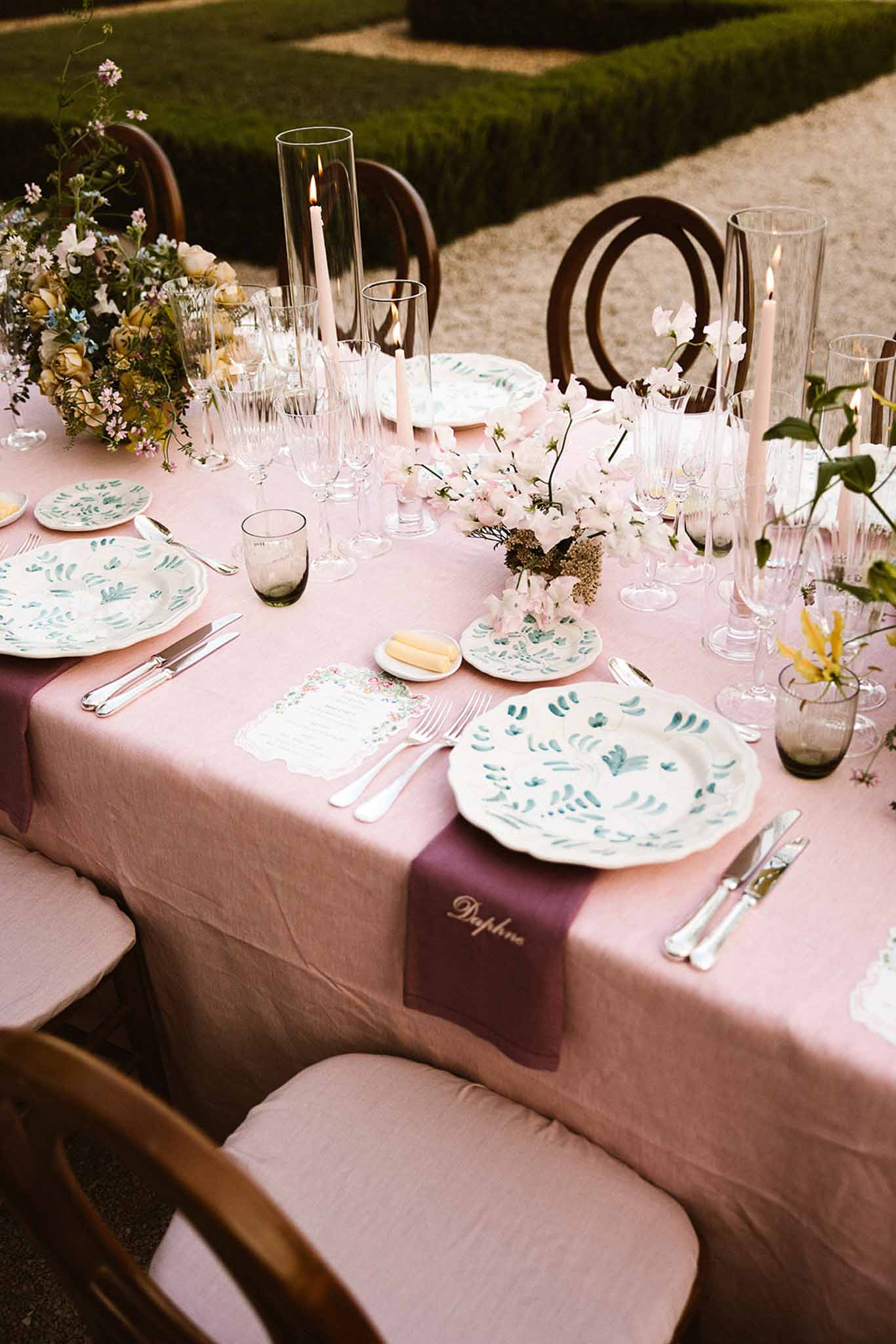 Blush linen with botanical painted plates, plum velvet ribbons, yellow roses, and smoky grey glassware