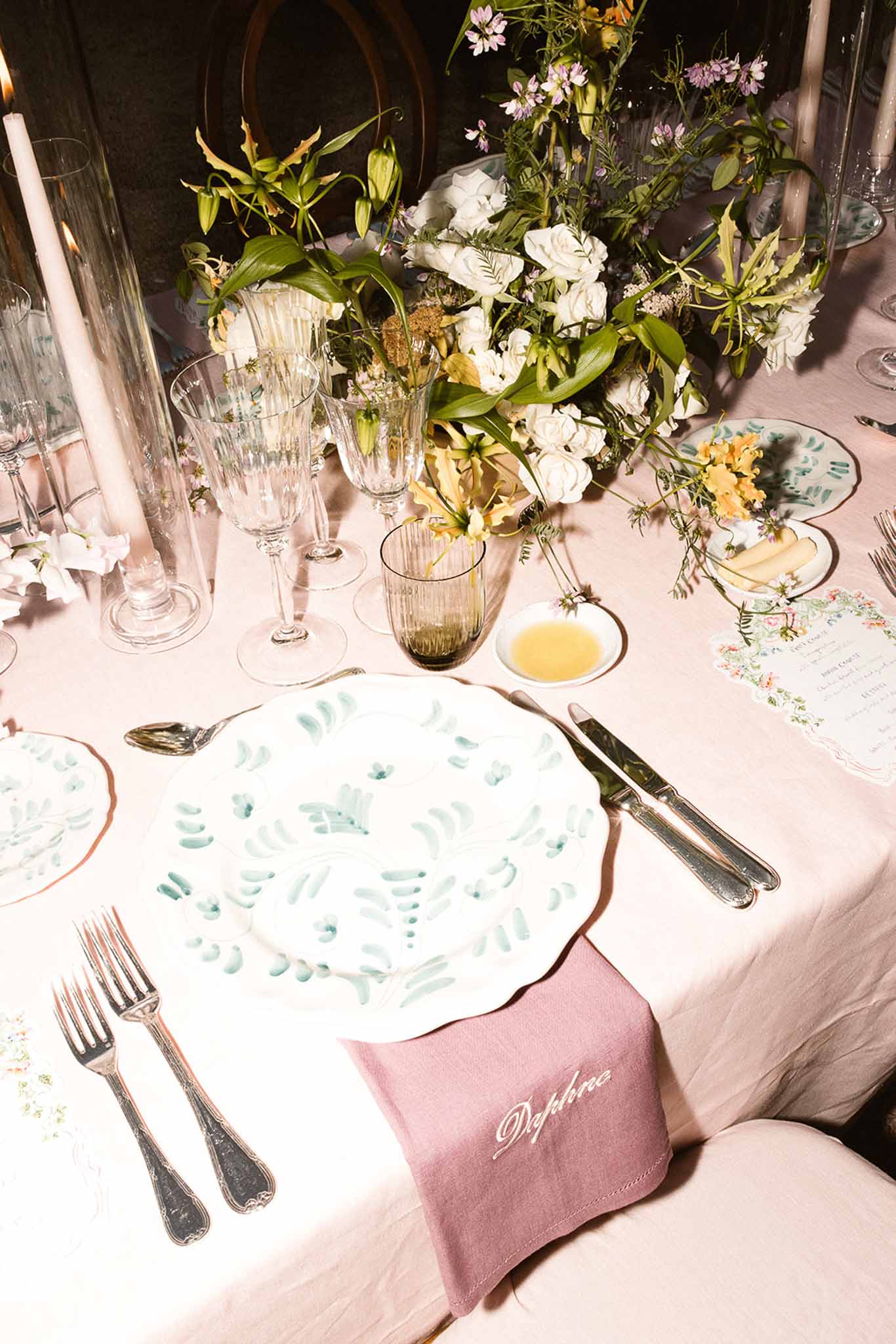 Blush linen place setting with botanical leaf plate, rose napkin, and wildflower centerpiece with tapers