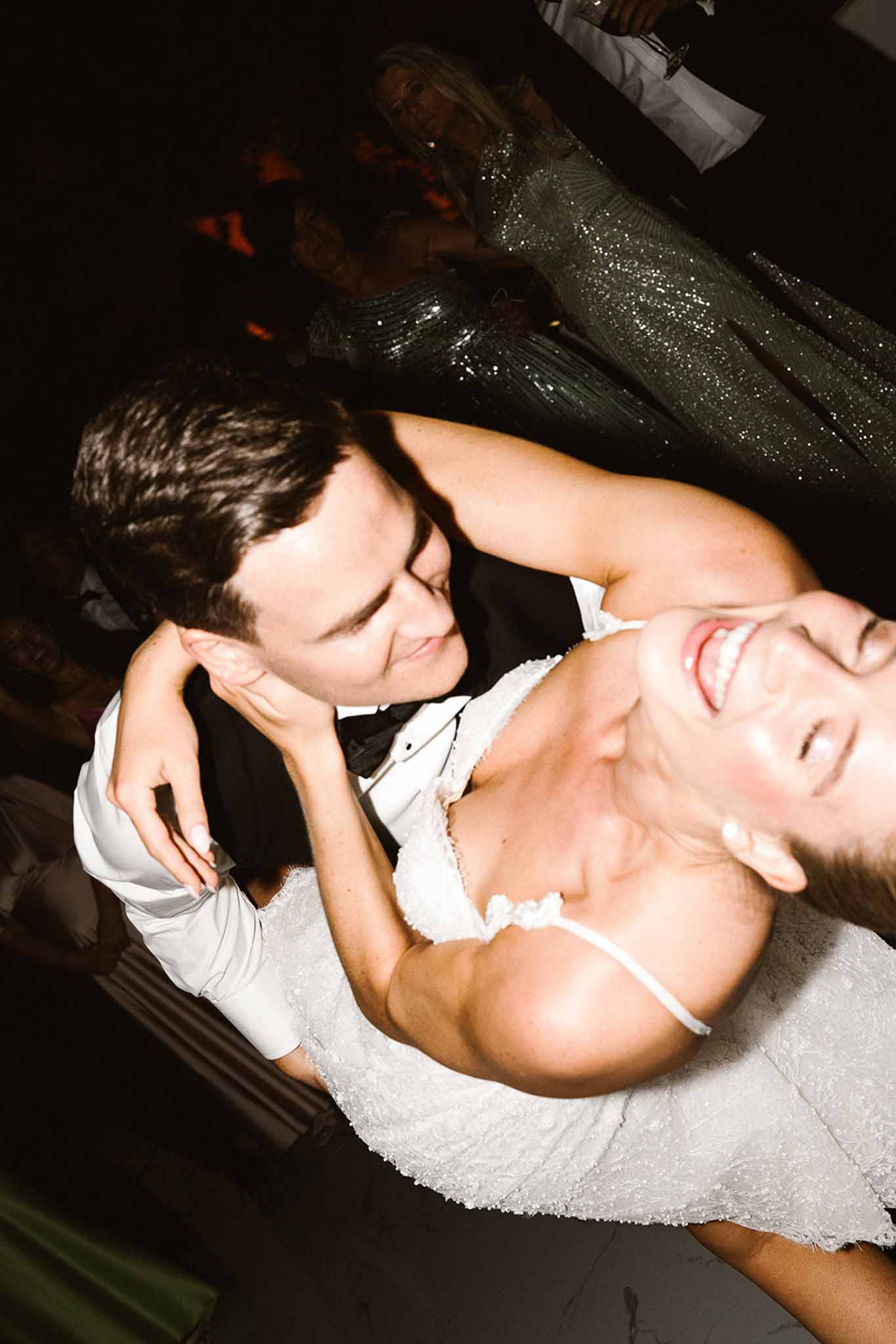 Bride and groom laughing while dancing at indoor reception captured from above at tilted angle