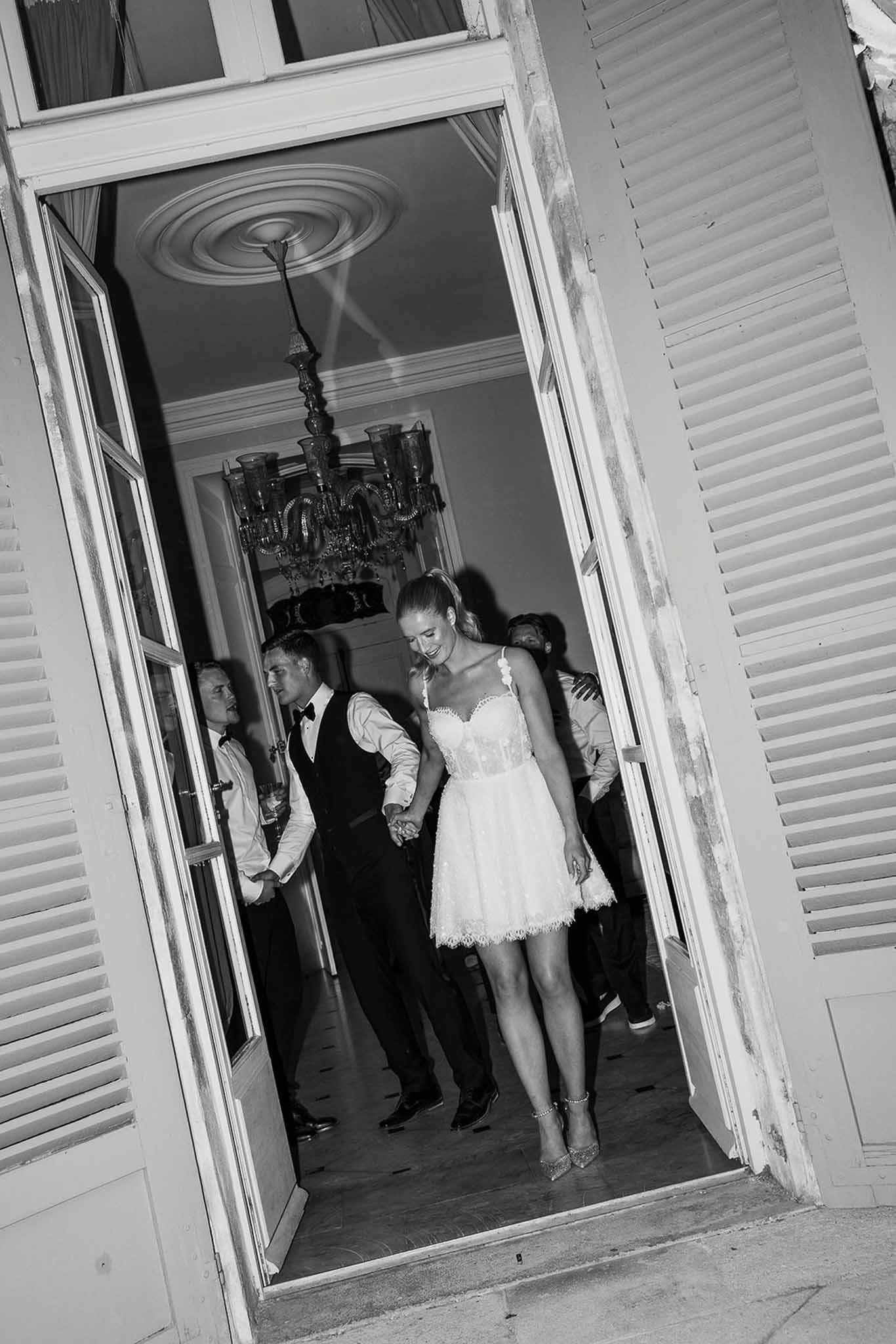 Black and white couple stepping through French doors bride in lace mini dress groom in waistcoat and bow tie