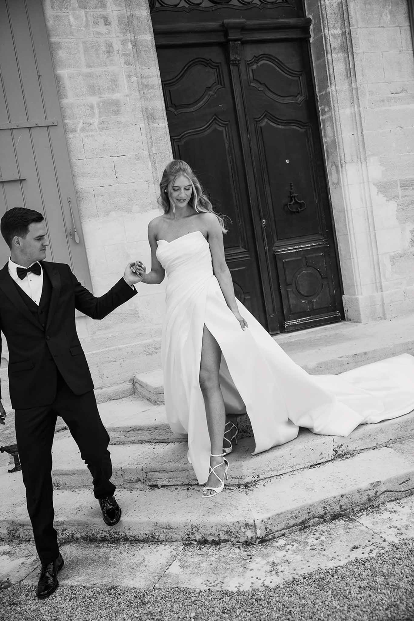 Black and white portrait of couple descending stone steps with bride's train cascading behind