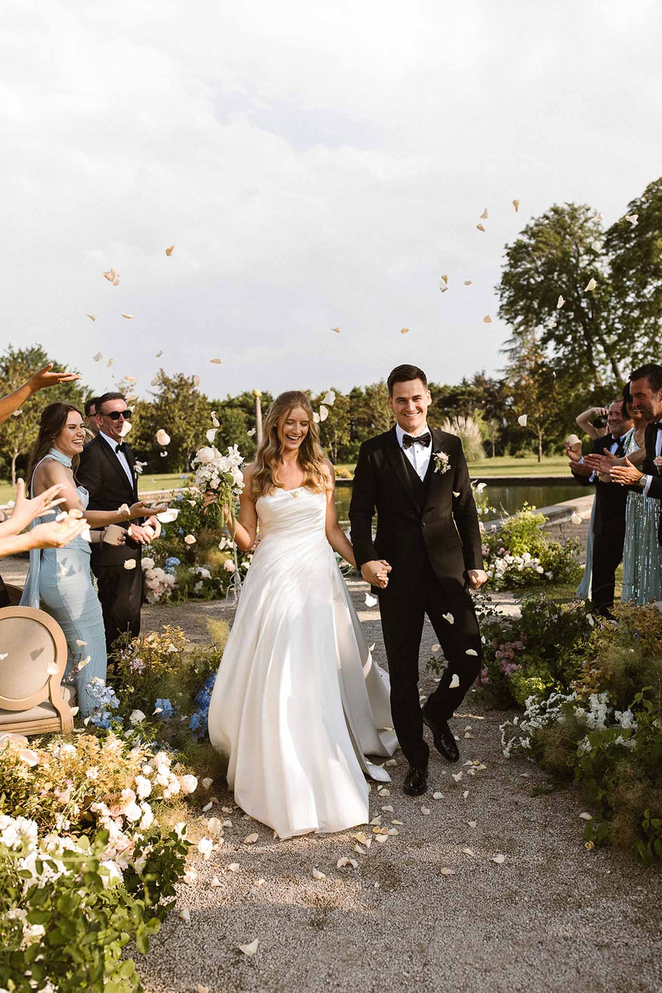 Petal toss recessional past white rose and blue hydrangea aisle arrangements with cheering guests