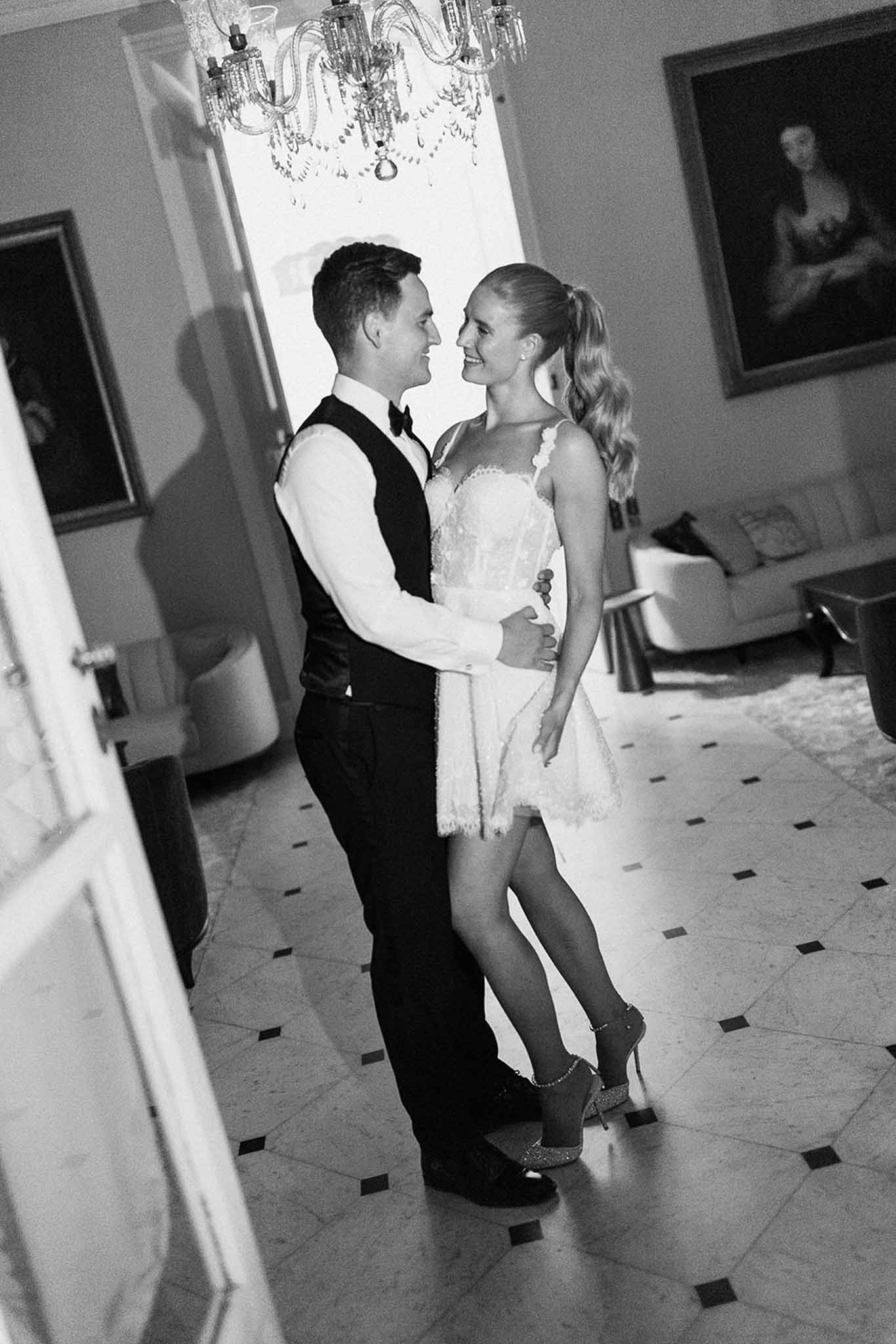 Black and white portrait of bride and groom embracing in chateau interior with chandelier and marble floor