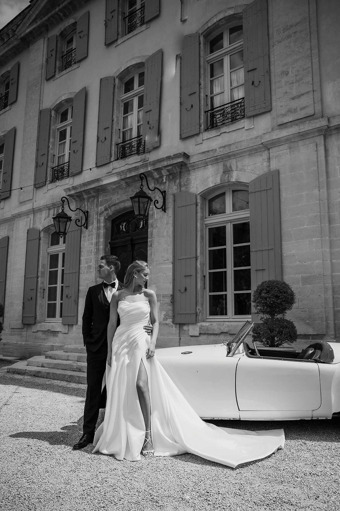 Black and white couple leaning on white vintage convertible before shuttered chateau entrance