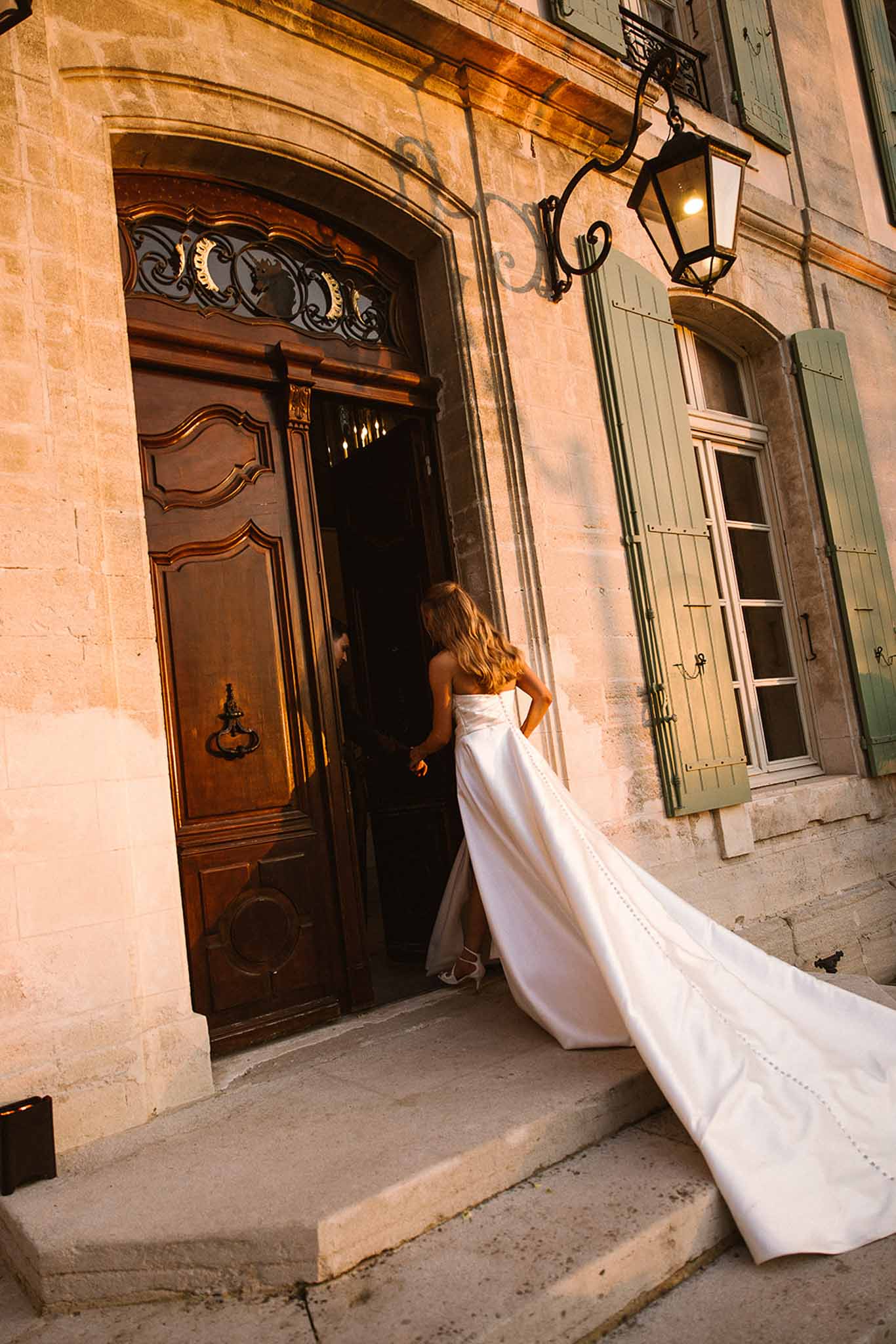 Bride entering chateau through ornate wooden doors with cathedral-length train fanning across stone steps