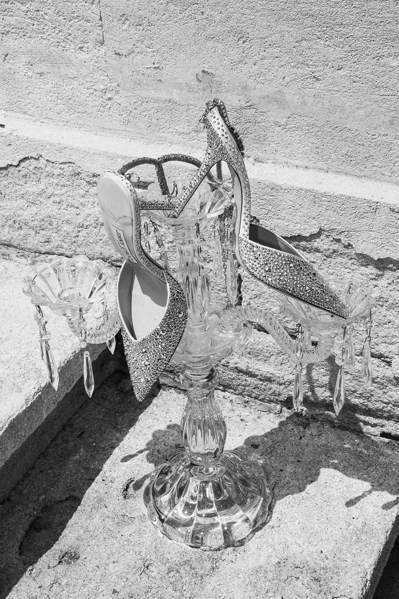 Black and white crystal-embellished Jimmy Choo slingback heels propped against crystal candelabra on stone