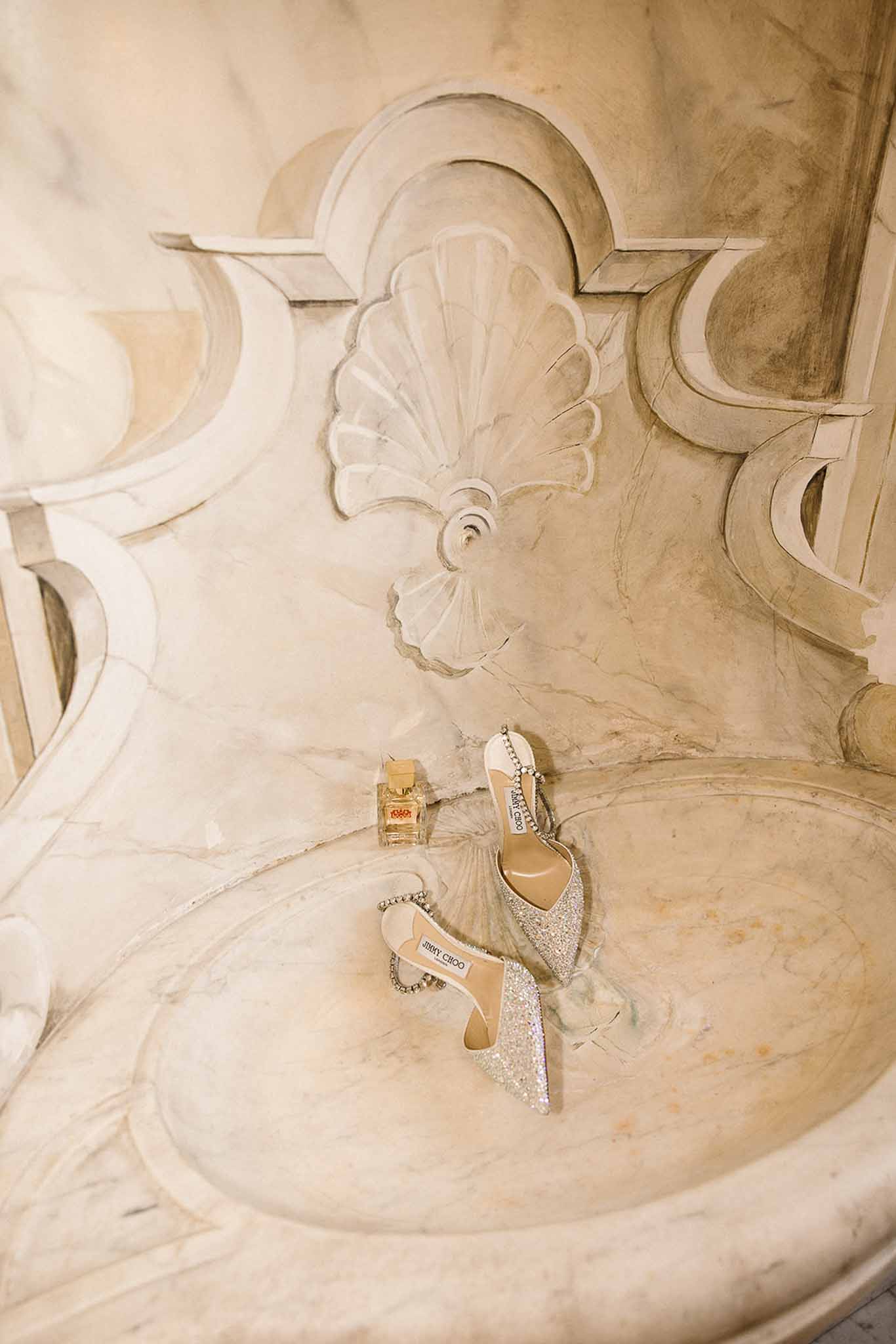 Crystal-embellished Jimmy Choo heels and gold Dolce Gabbana perfume in carved marble fountain basin
