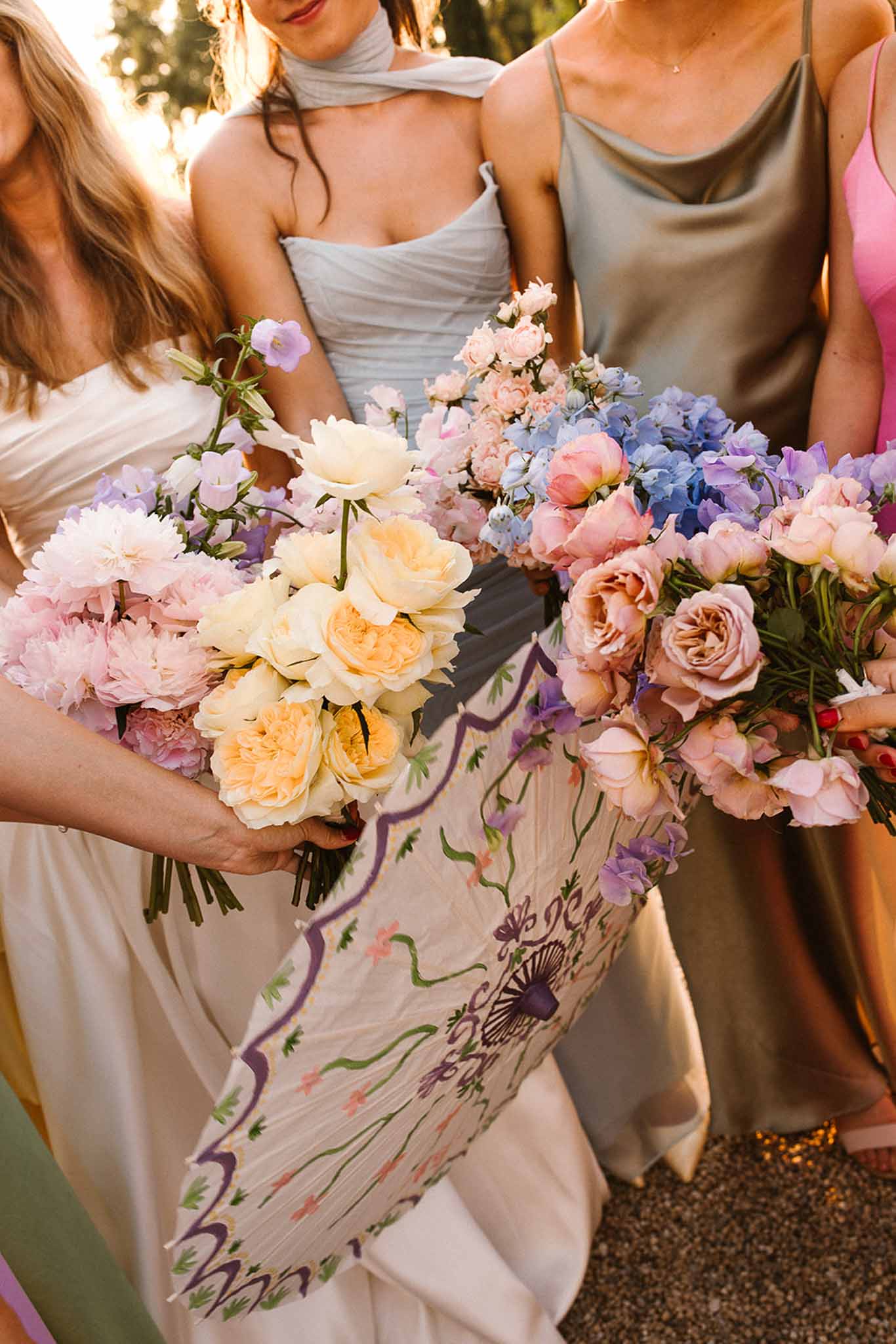 Four bridesmaids in mismatched pastel dresses holding bouquets of peonies, roses, and hydrangeas