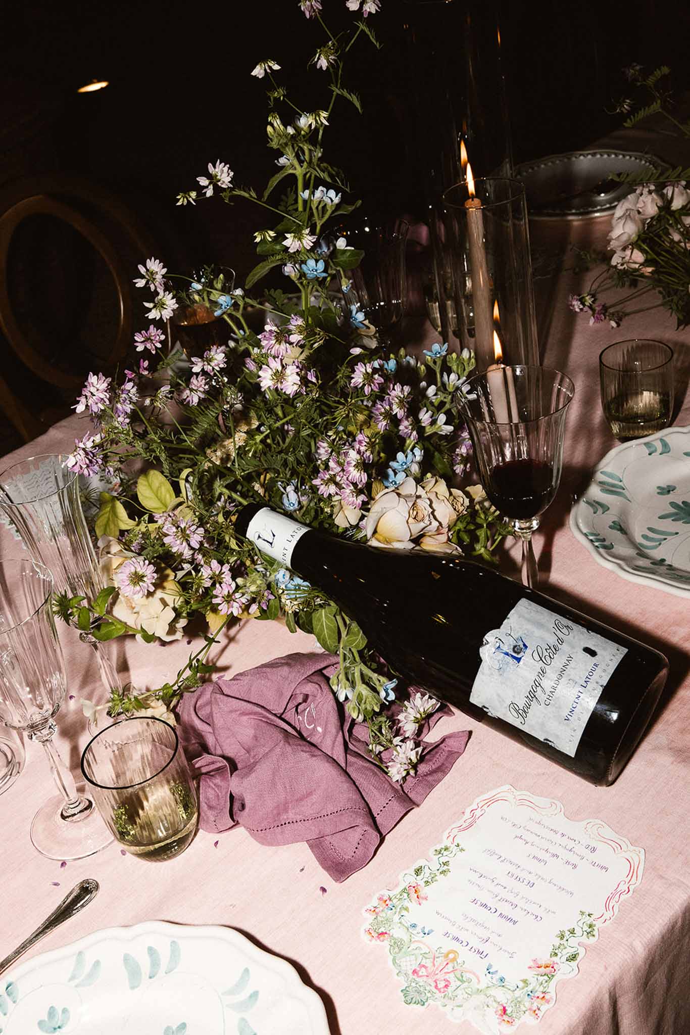 Wedding reception table with blush linen, lavender and cream floral arrangement, taper candles, wine bottle and monogramme...