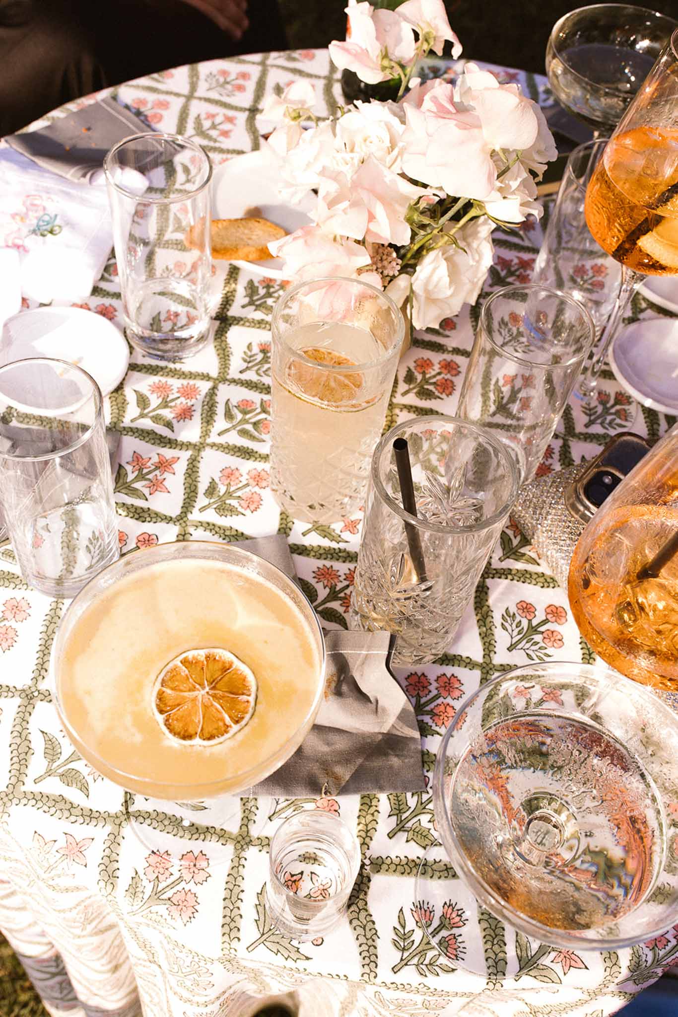 Cocktail table with citrus sour, rose wine, and sweet pea bouquet on green-and-coral printed tablecloth